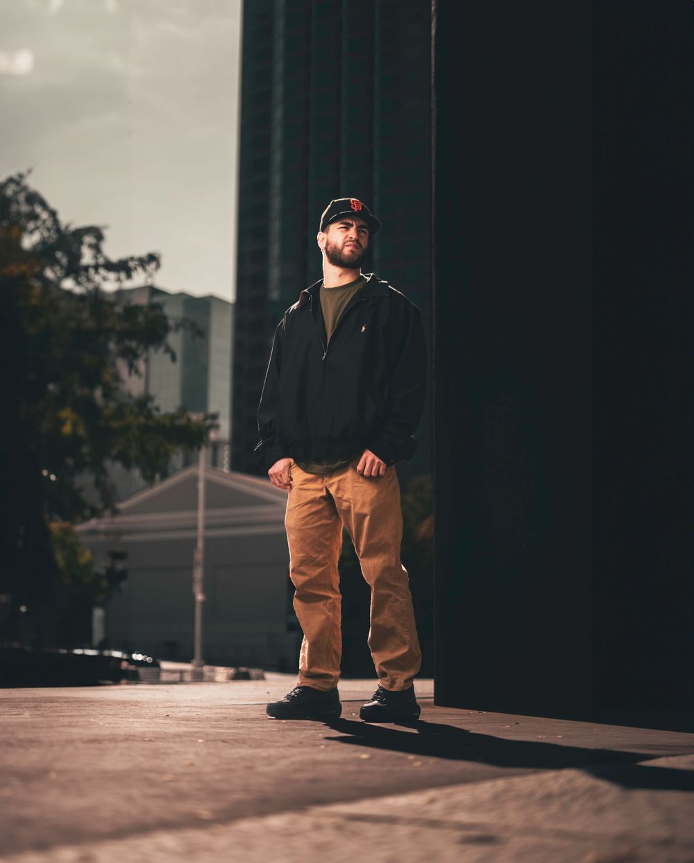 Urban portrait of someone in casual attire standing against a dark building backdrop.
