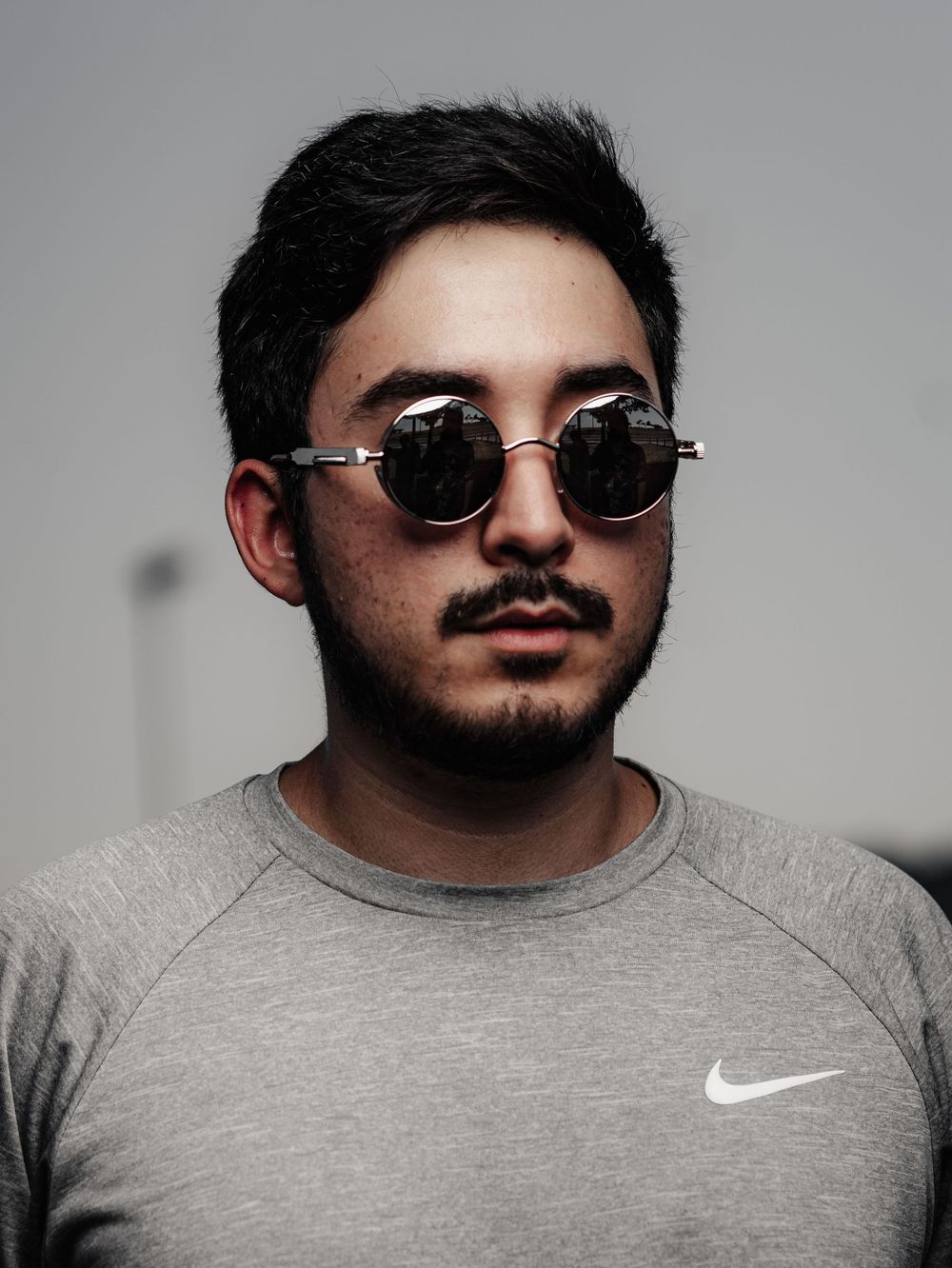 Portrait featuring round sunglasses and Nike shirt against gray background.
