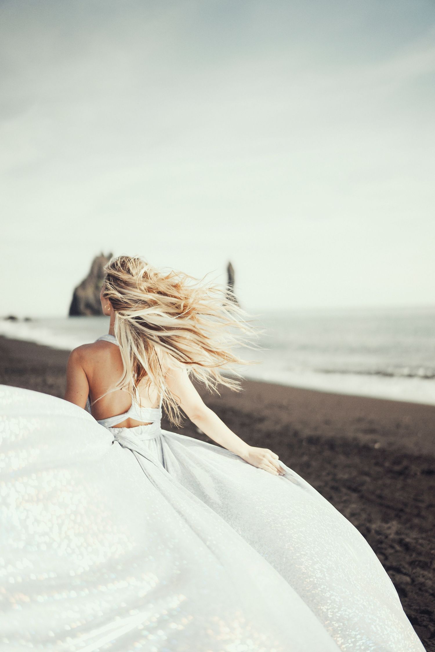 Person with flowing blonde hair in white dress on beach with dreamy atmosphere.