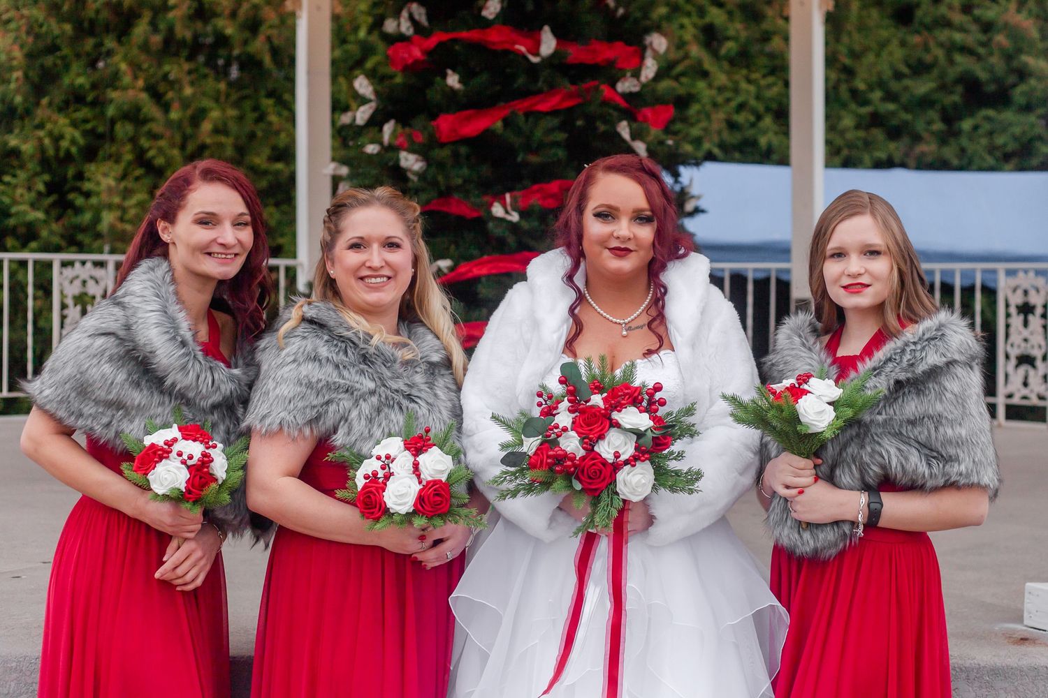 Wedding party poses outdoors wearing red dresses and holding floral bouquets.