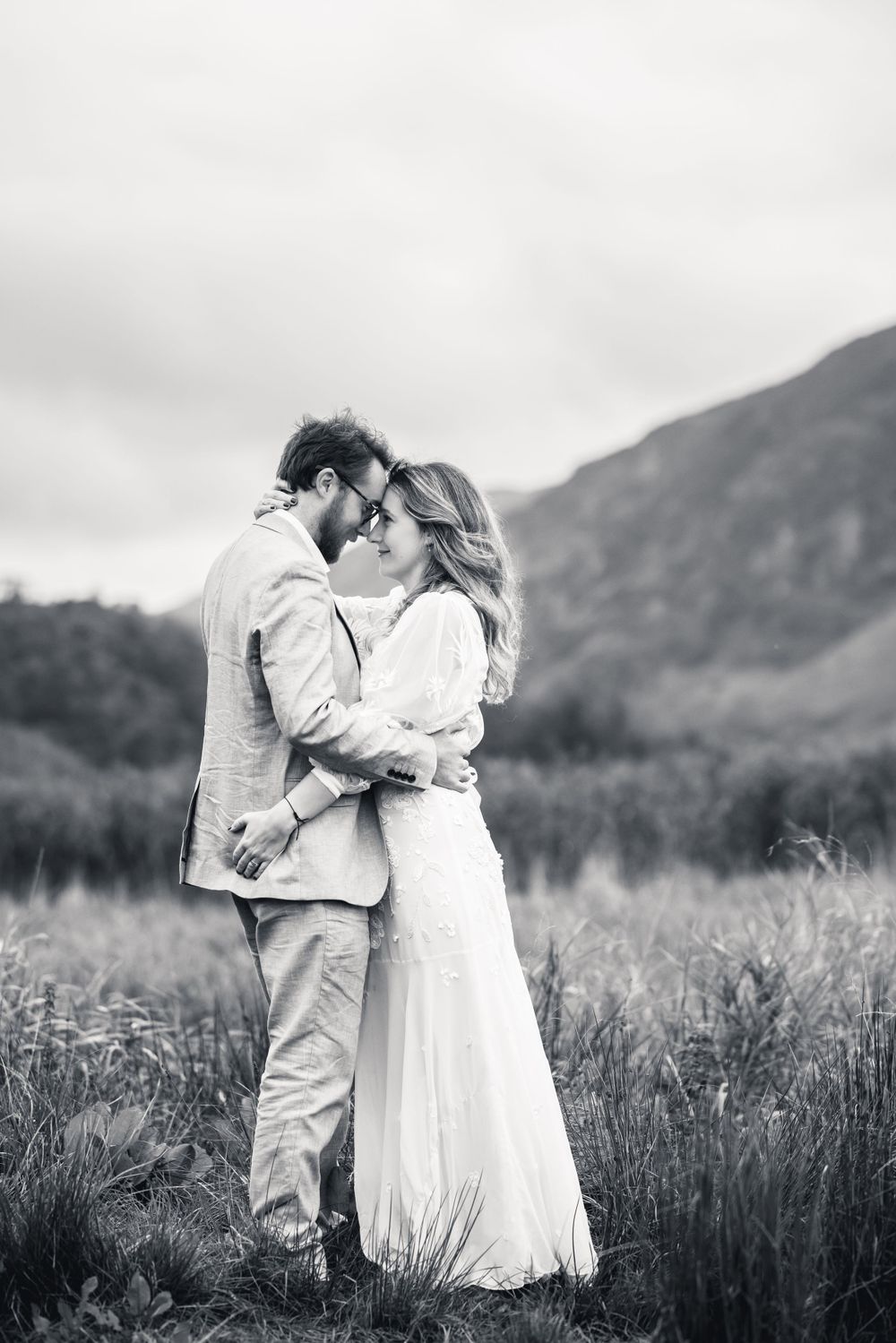 Black and white photo of couple embracing in mountain meadow.