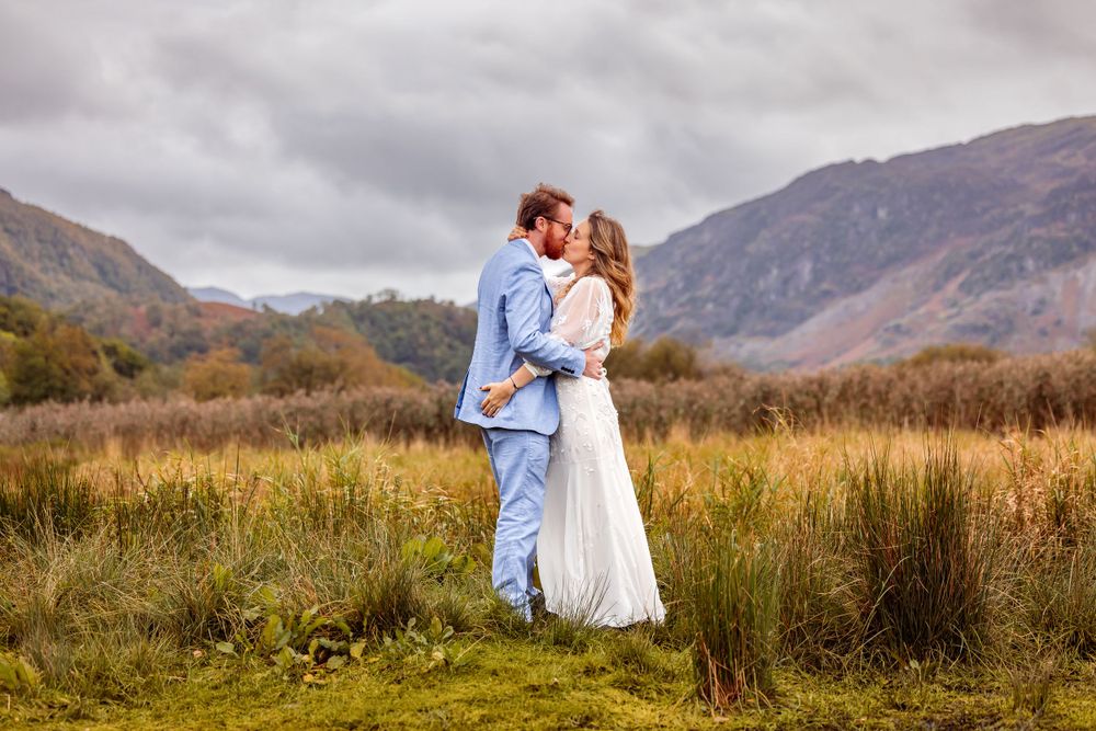 Couple in formal wear embracing in mountain valley with dramatic clouds.