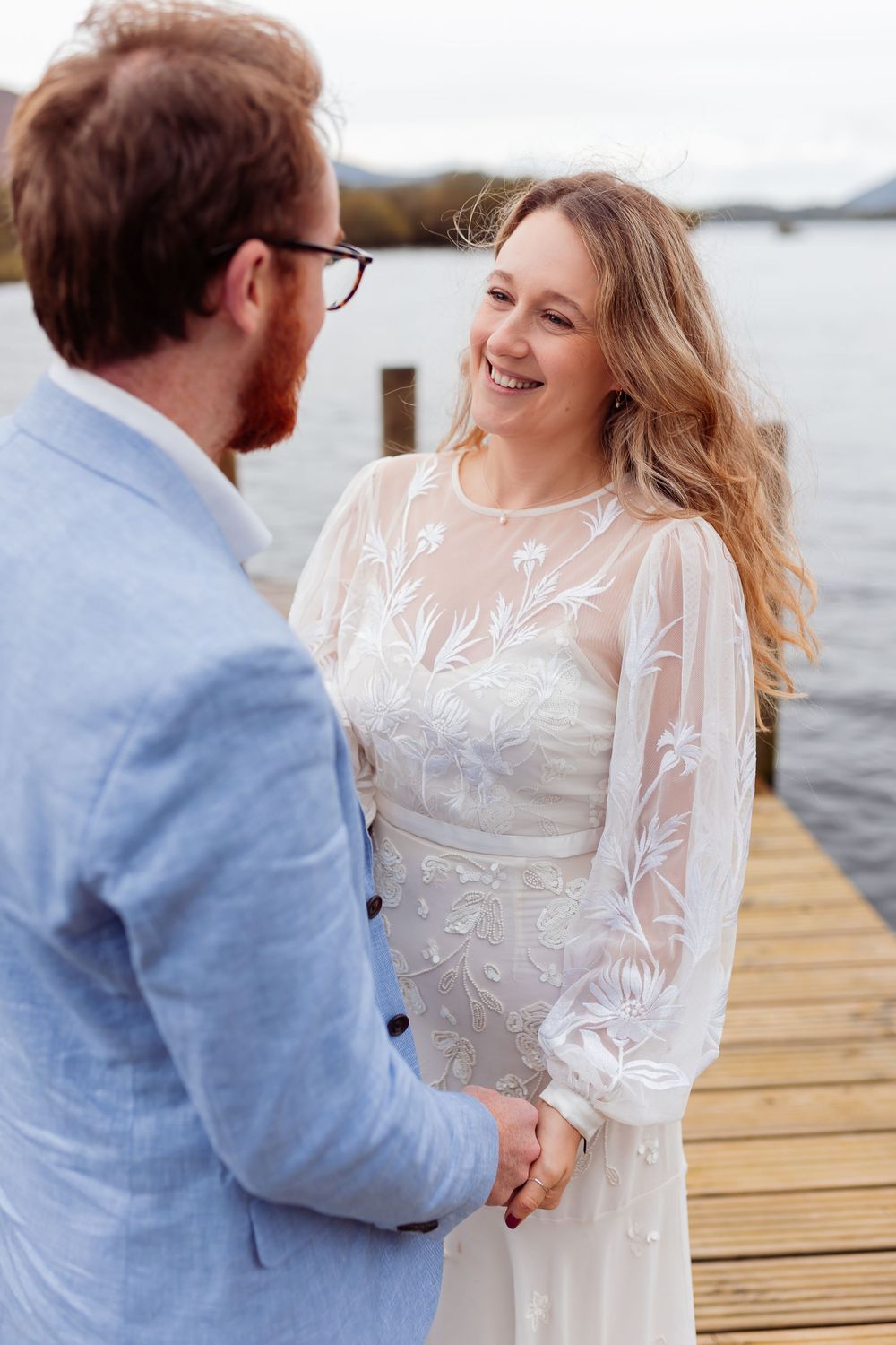 A joyful moment shared between a couple on a lakeside dock wearing wedding attire.