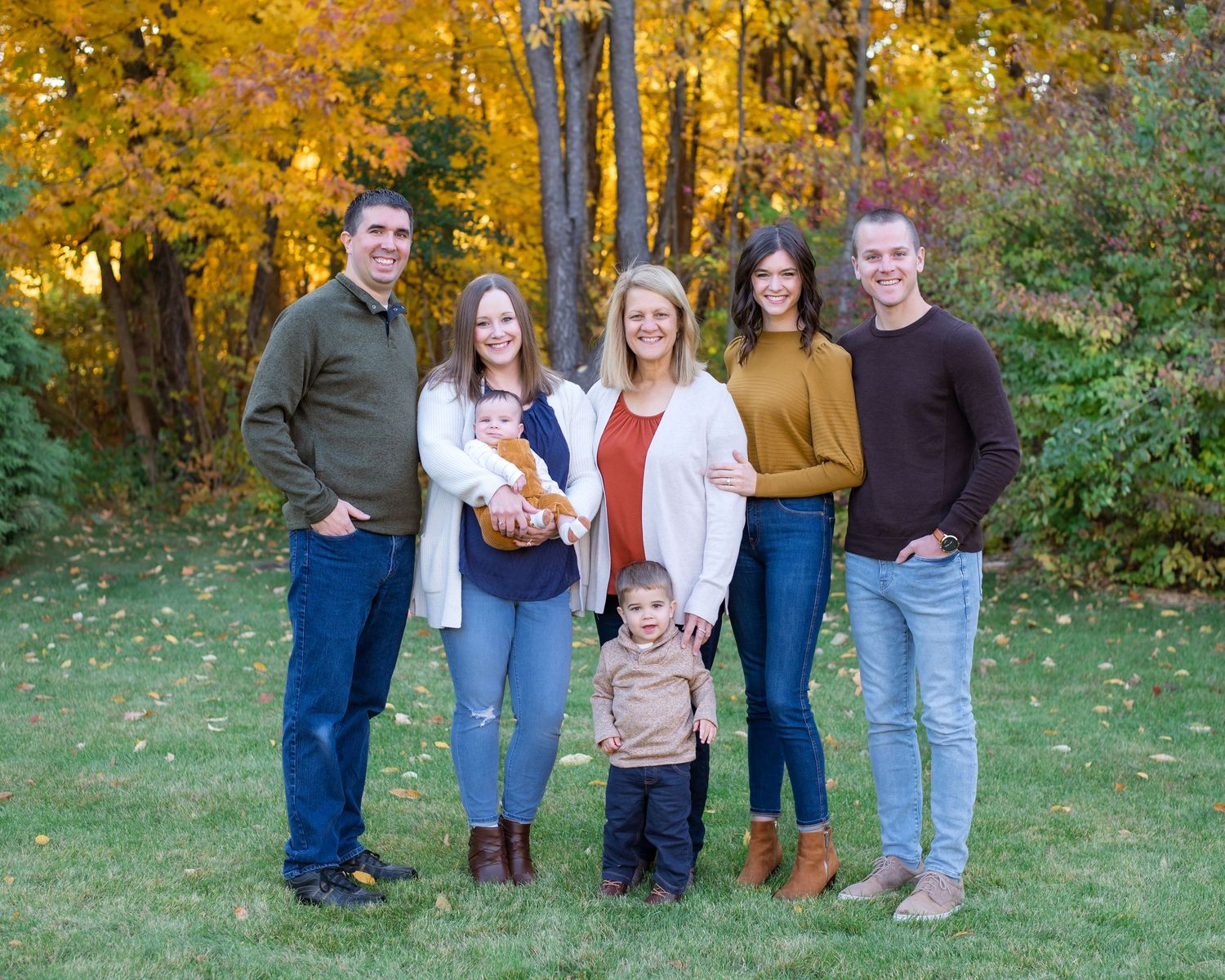 Family group poses together on grass with beautiful golden autumn trees behind them.
