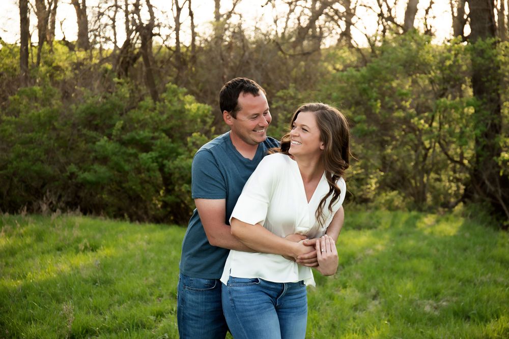 A joyful couple embraces while laughing together in a spring garden setting.