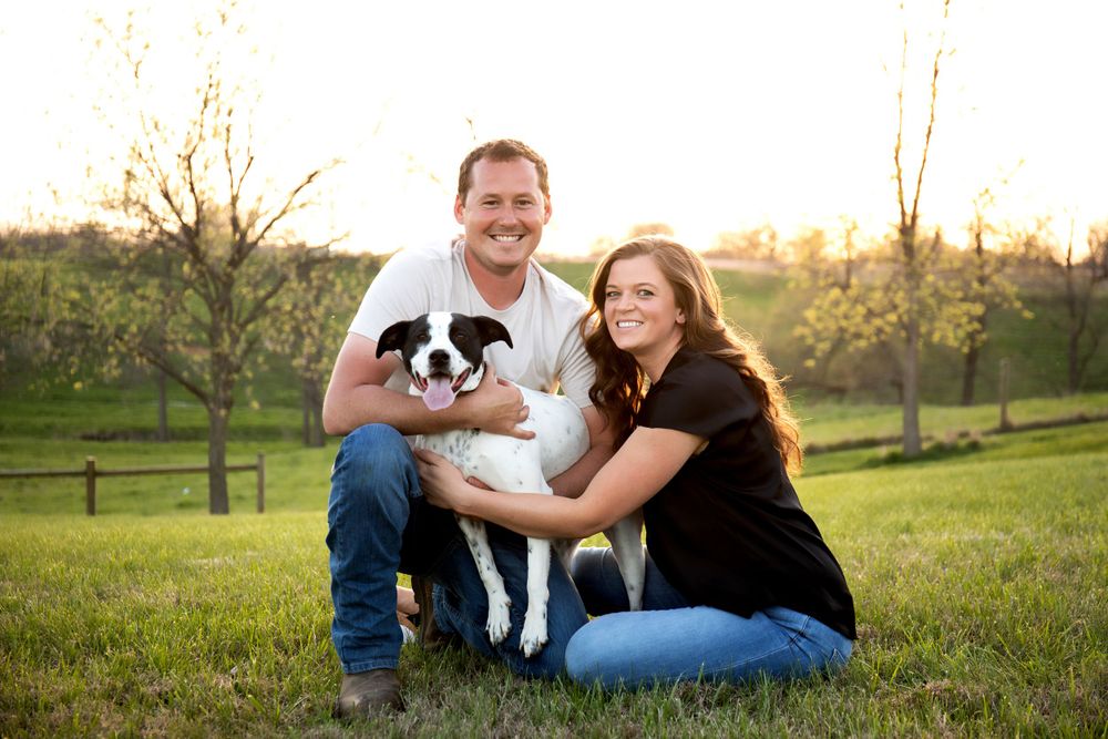 A couple poses with their black and white border collie dog in a green field.