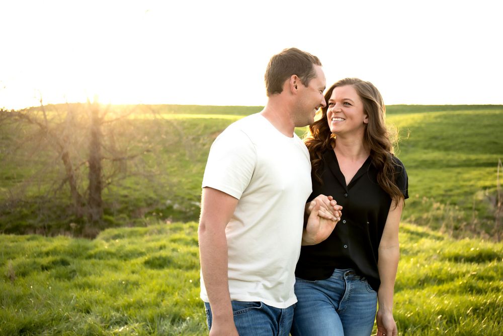 A joyful couple shares a laugh together in a green field at sunset.