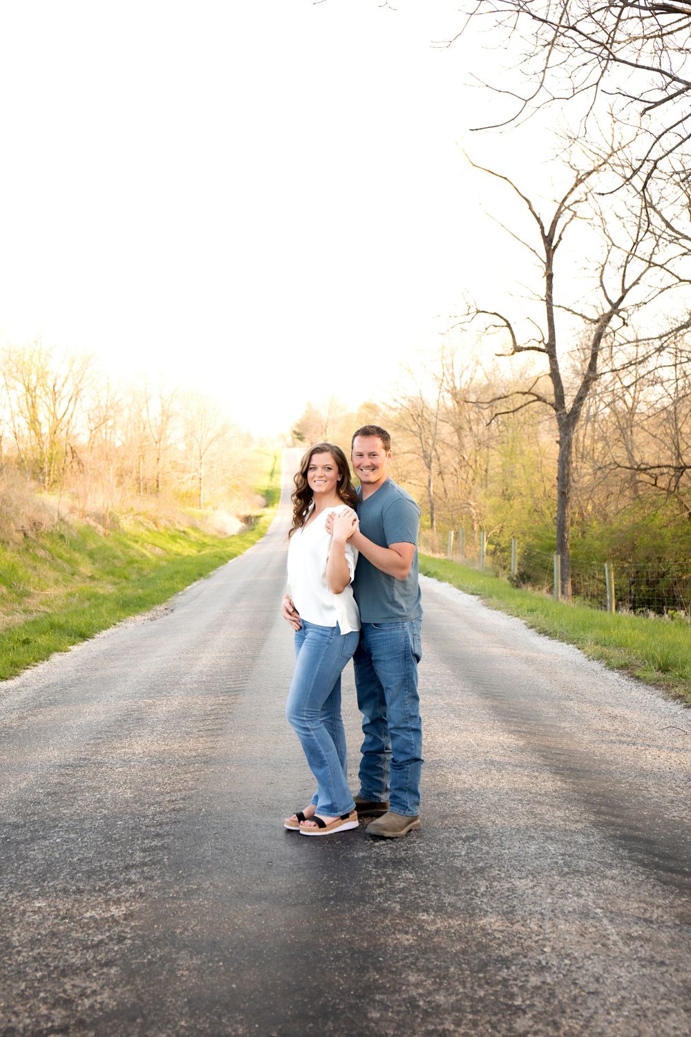 A couple stands together on a rural road during golden hour for a romantic portrait.