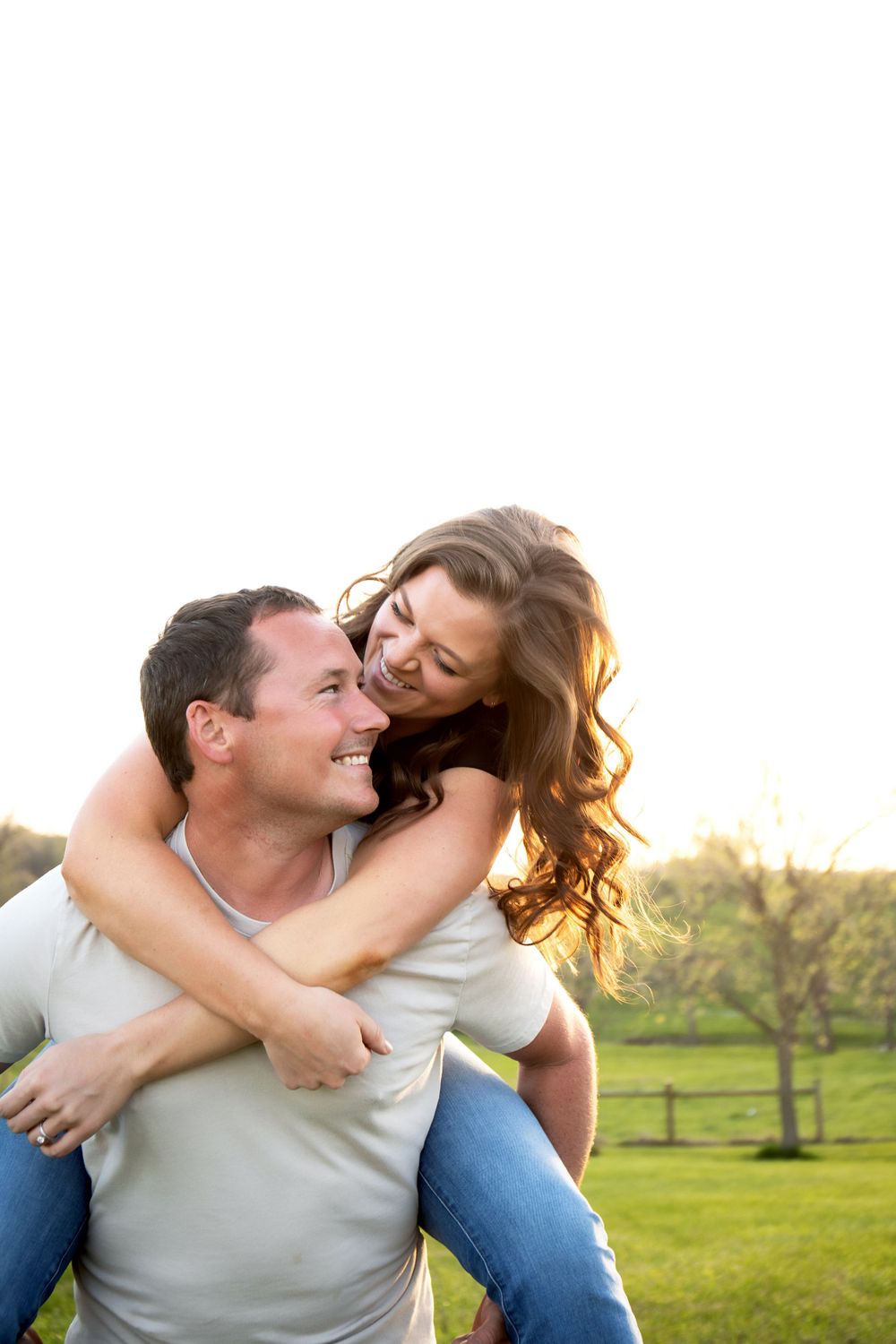 A playful piggyback ride moment captured between a couple in a sunny field.