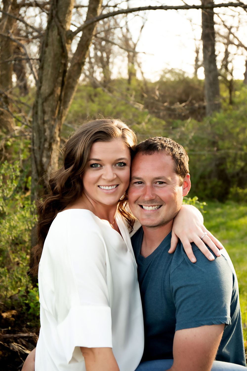 A couple poses close together for a portrait in a natural wooded setting.