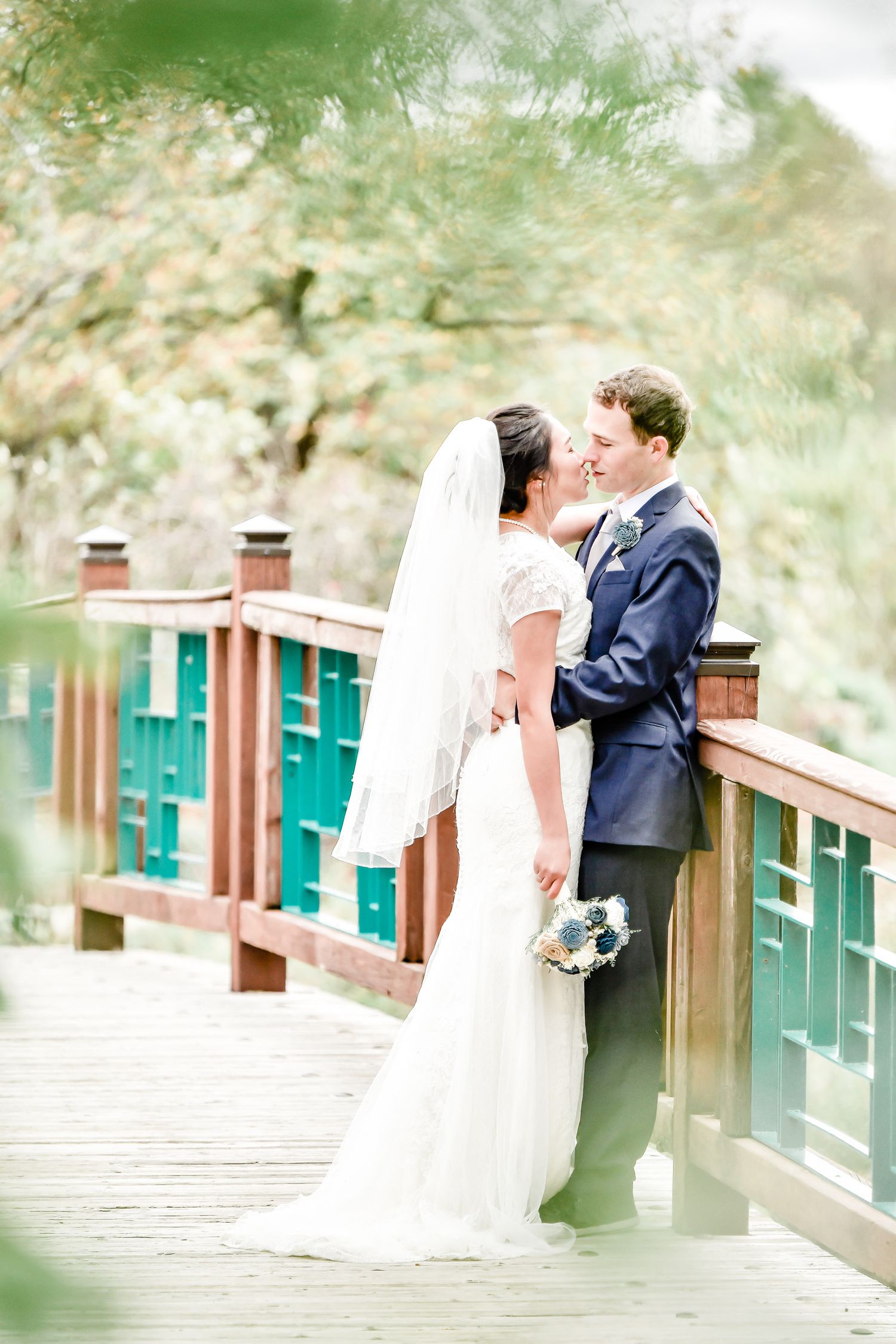 A couple shares an intimate moment on a wooden bridge with green scenery in the background during their wedding day by Stephanie Coulter Pho