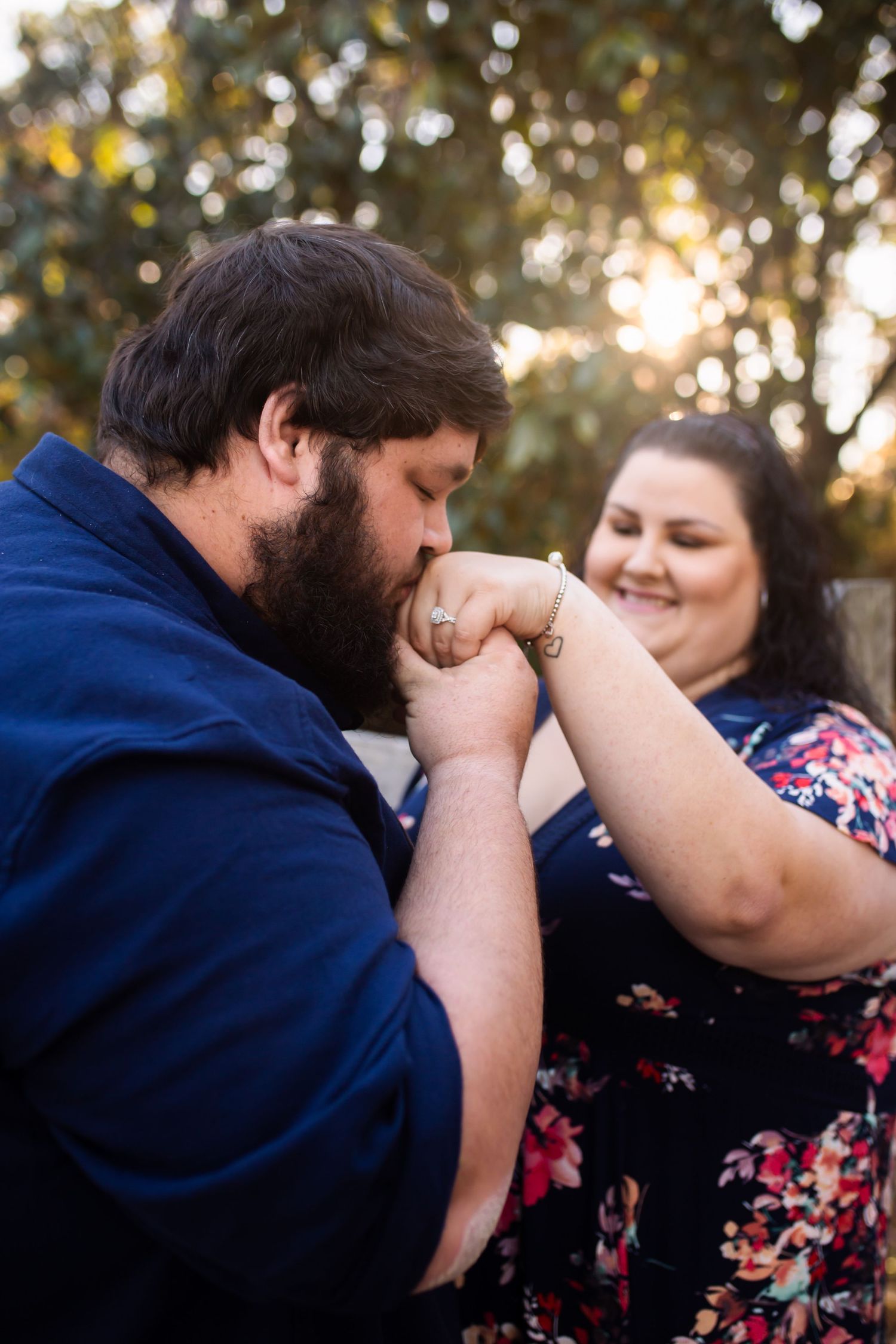 A romantic engagement photo session moment captured in golden hour lighting among trees.