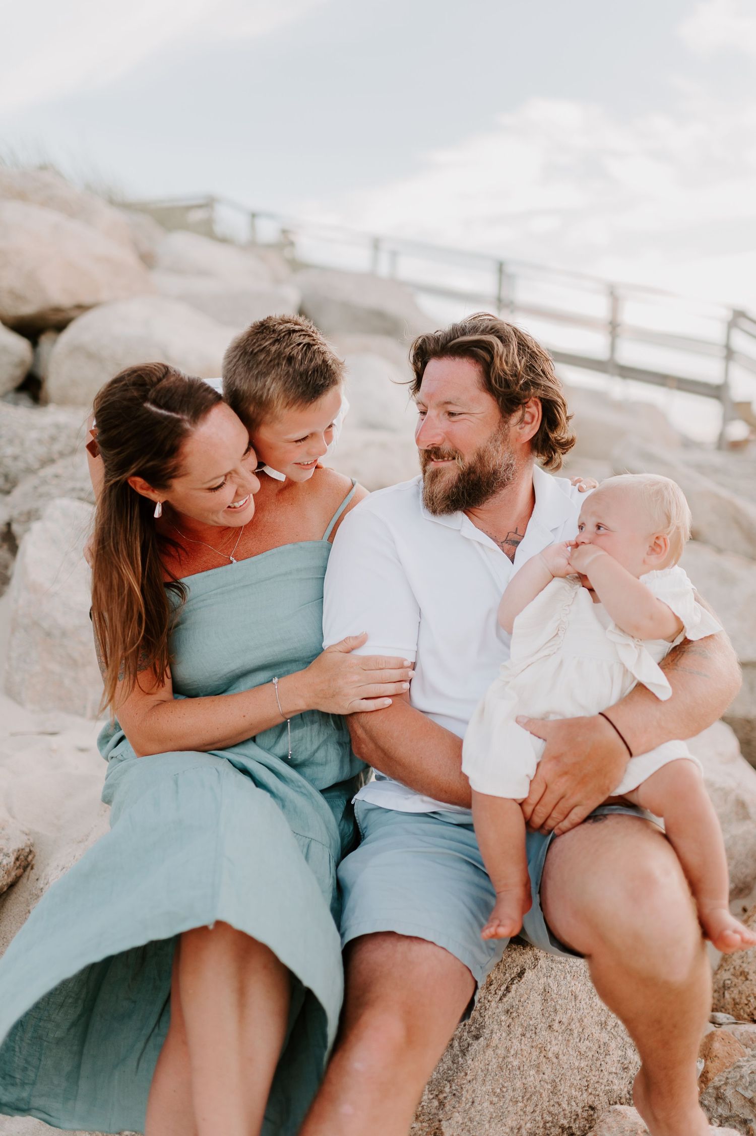 Family wearing blue and white outfits laughing together on a beach during a casual photo session.