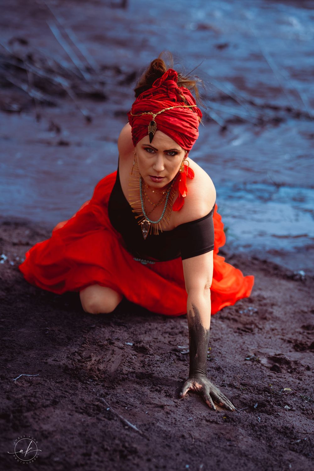 Figure in red dress and headwrap poses dramatically on dark rocky surface.