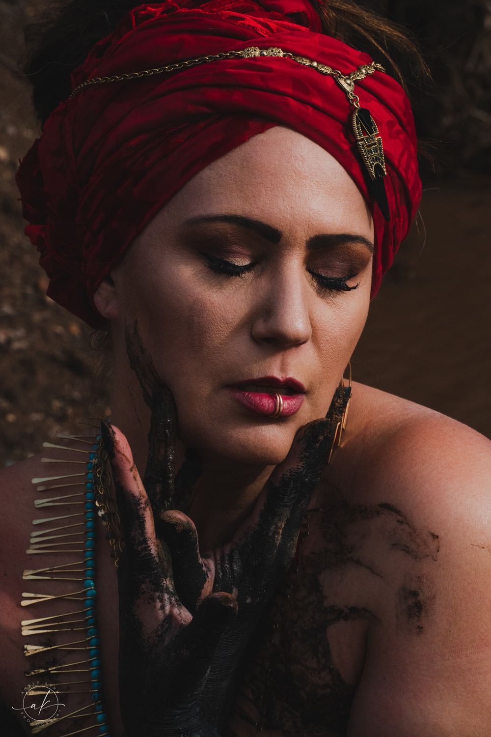 Moody portrait featuring red turban with chain details and dramatic makeup in dark setting.