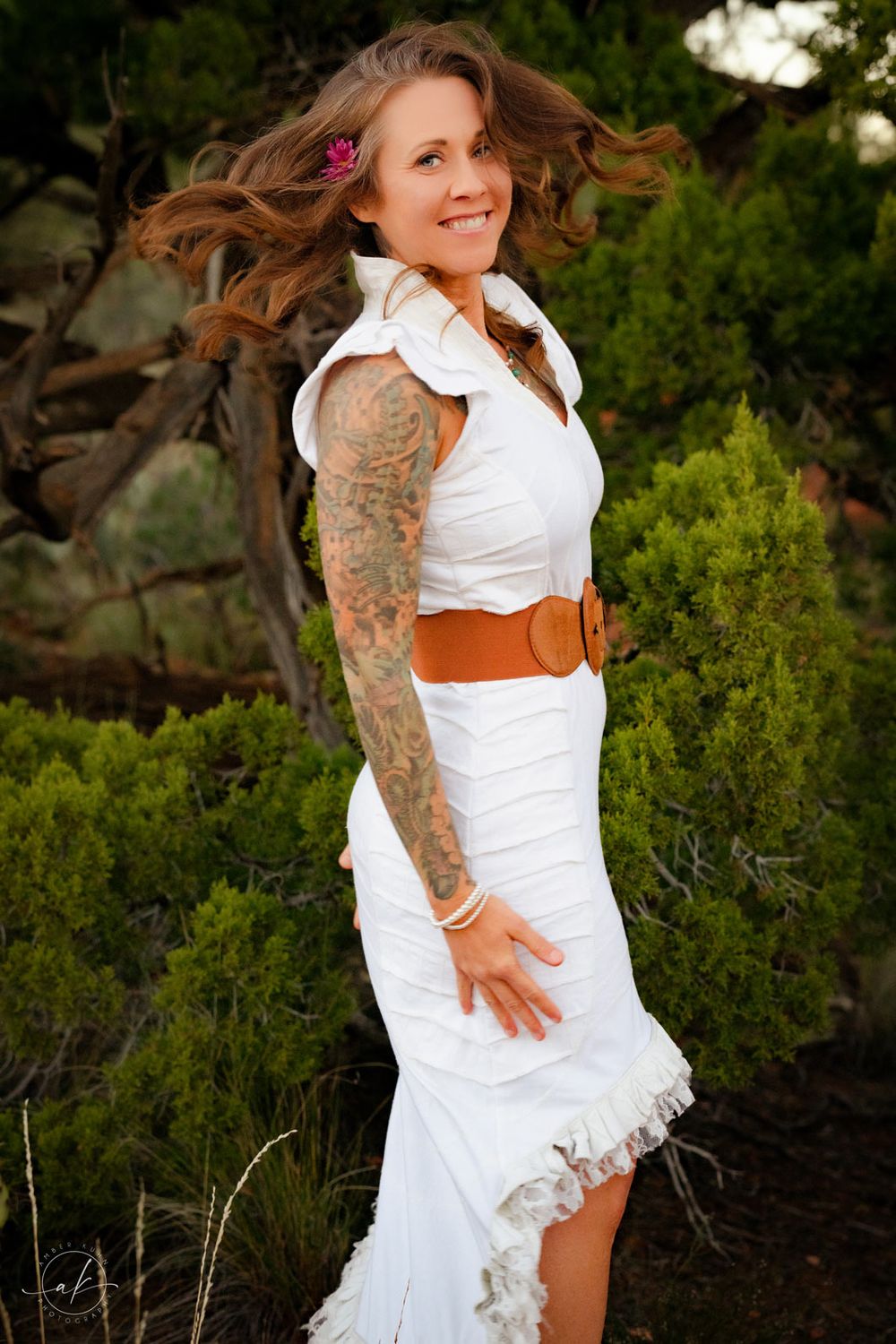 Full length portrait of woman in white dress with sleeve tattoo posing among Sedona desert vegetation.