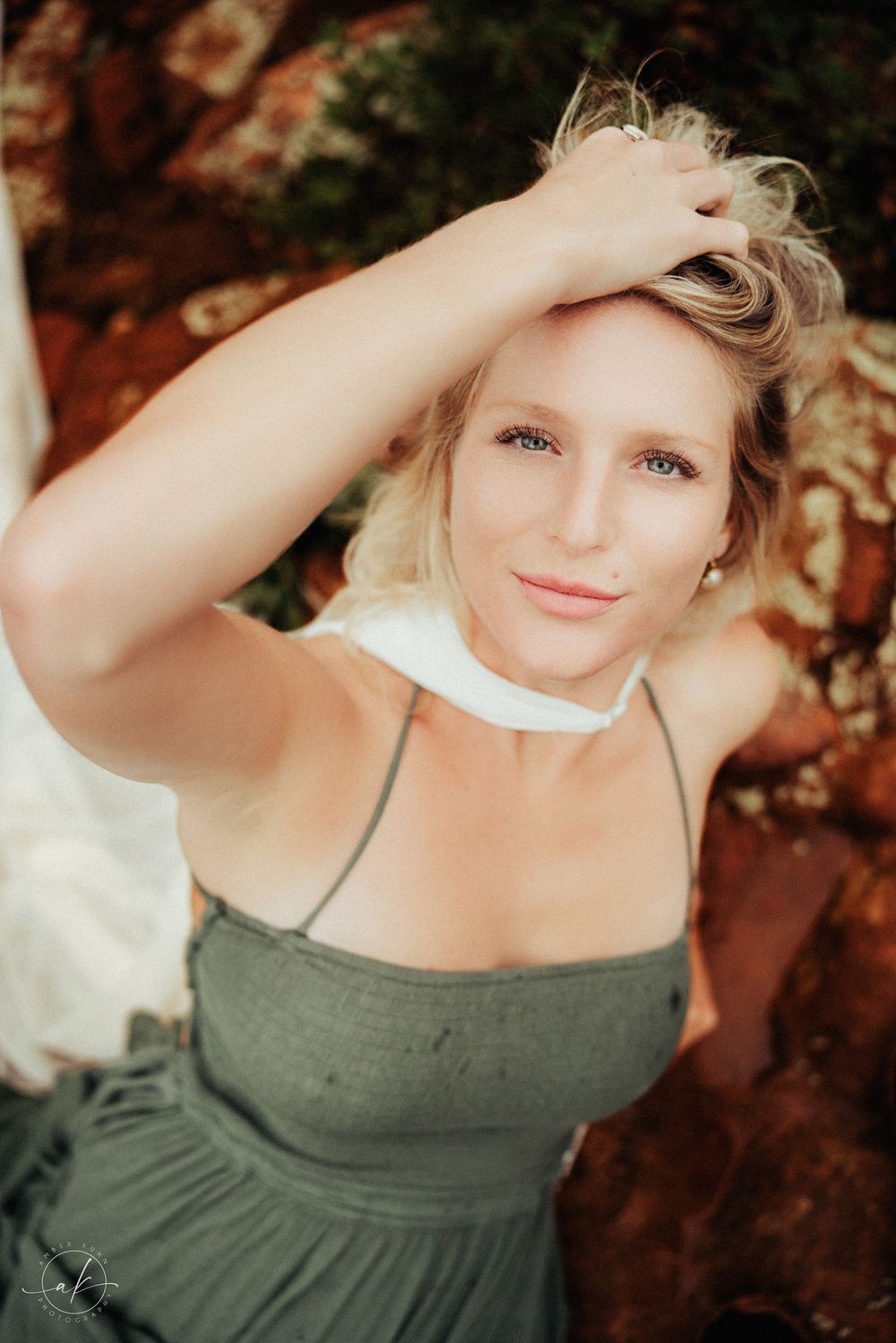 Soft portrait against Sedona red rocks wearing olive dress and white collar in warm sunlight.