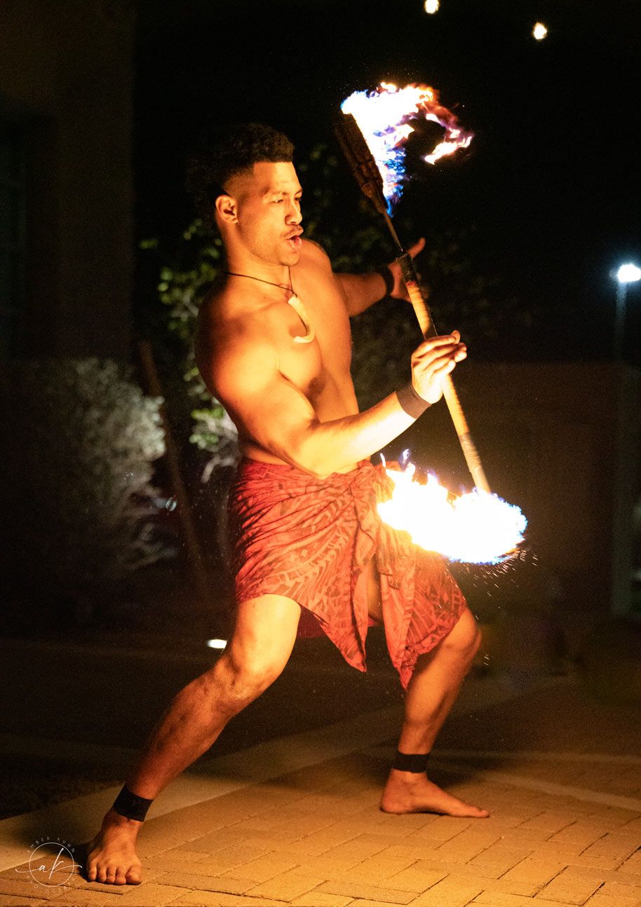 Polynesian fire dancer performs with flaming torches in traditional costume at night.