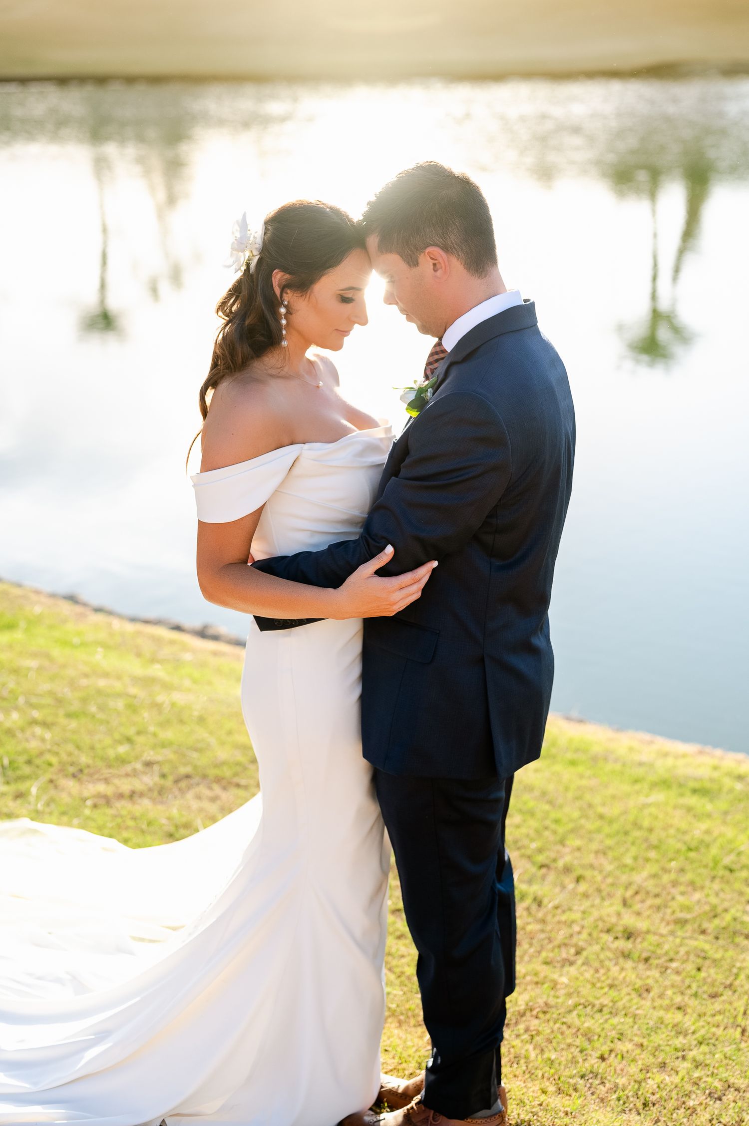 A romantic moment between newlyweds by a serene lake at sunset.
