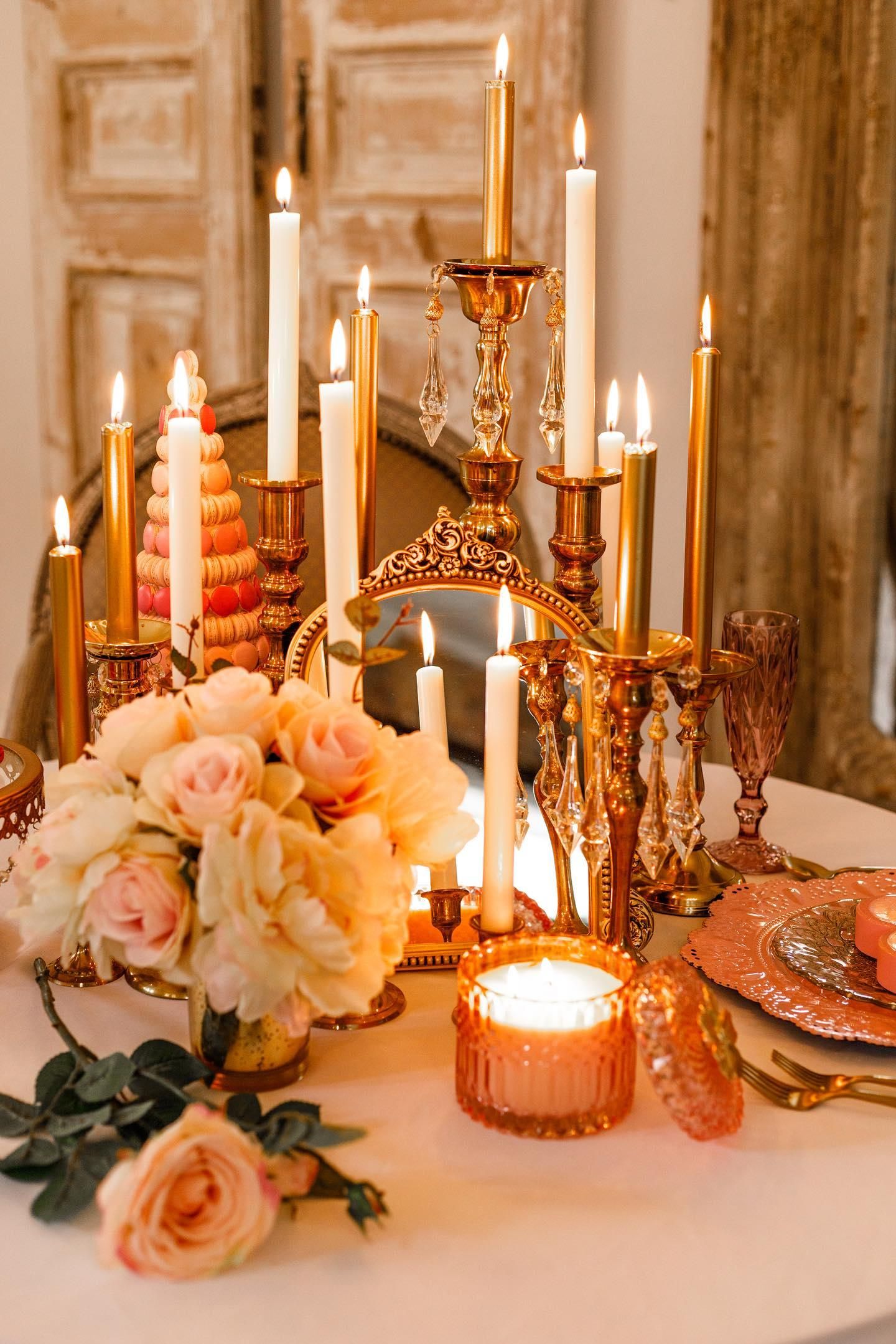 Romantic table setting with lit candles, peach roses, and amber glassware creating a warm golden ambiance.