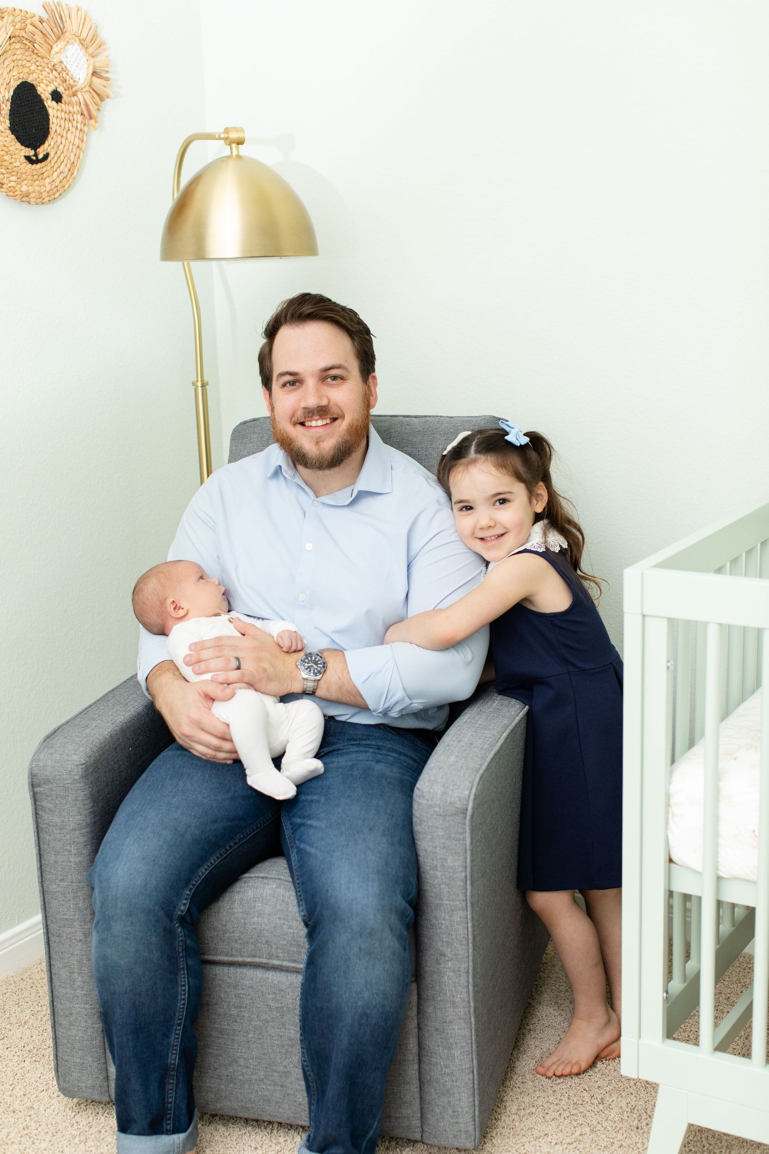 Family shares tender moment together in grey armchair next to gold floor lamp and koala wall decor.