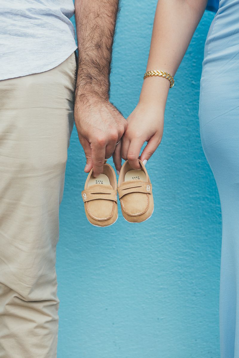 a close up view of a couple standing right next to each other holding baby shoes against a blue backdrop