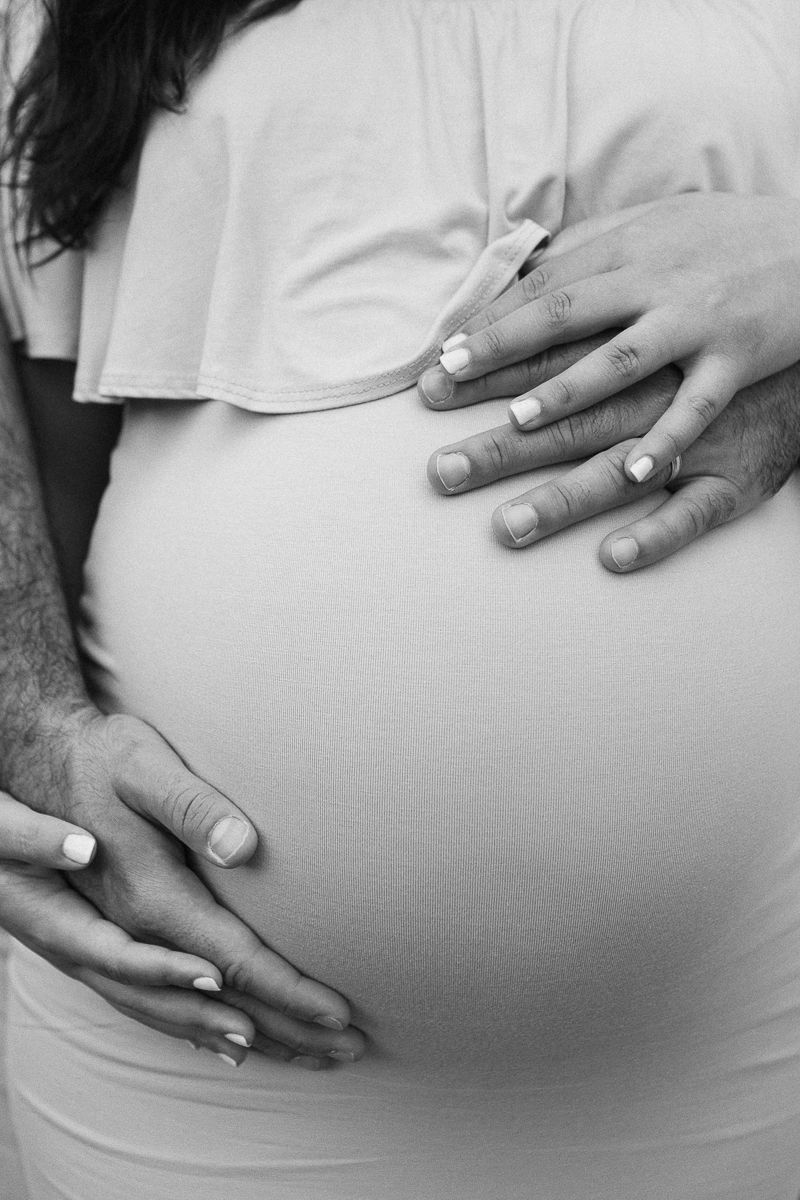 a close up view of a couple's hands around a pregnant belly in black and white, photo by Paula Ortiz NYC family photos