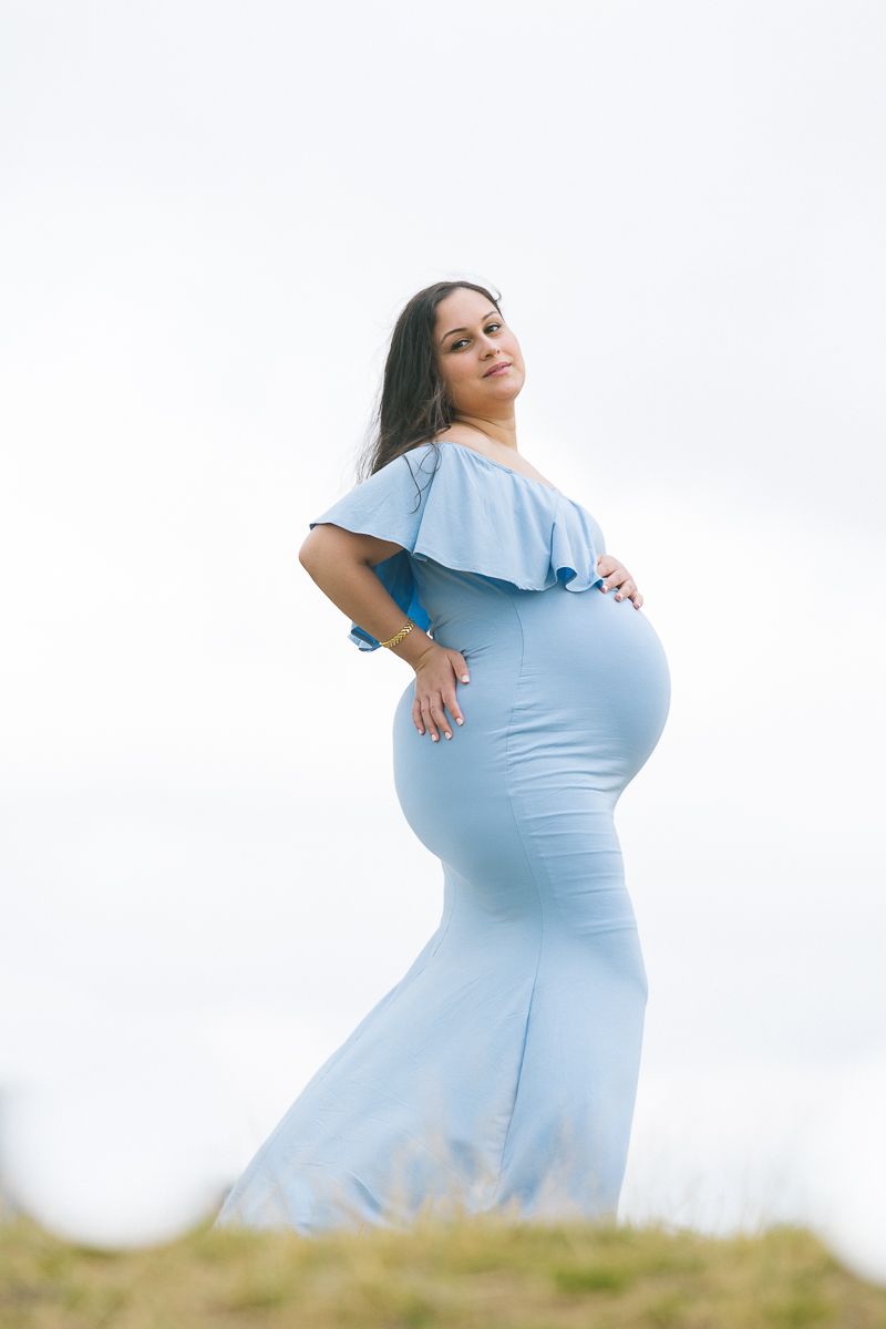 a pregnant woman wearing a blue dress stands in a profile pose during her maternity session by NYC maternity photography