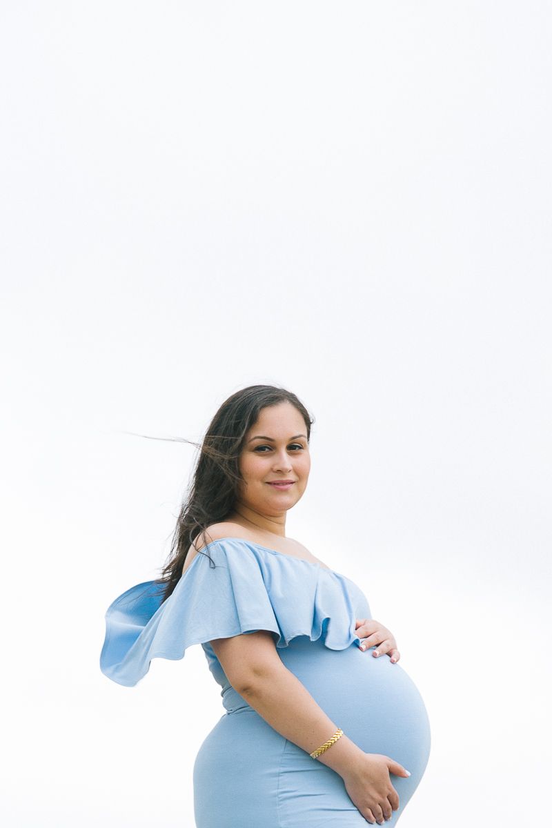 a half body view of a pregnant woman in a blue dress against a white background captured by Paula Ortiz NYC Maternity