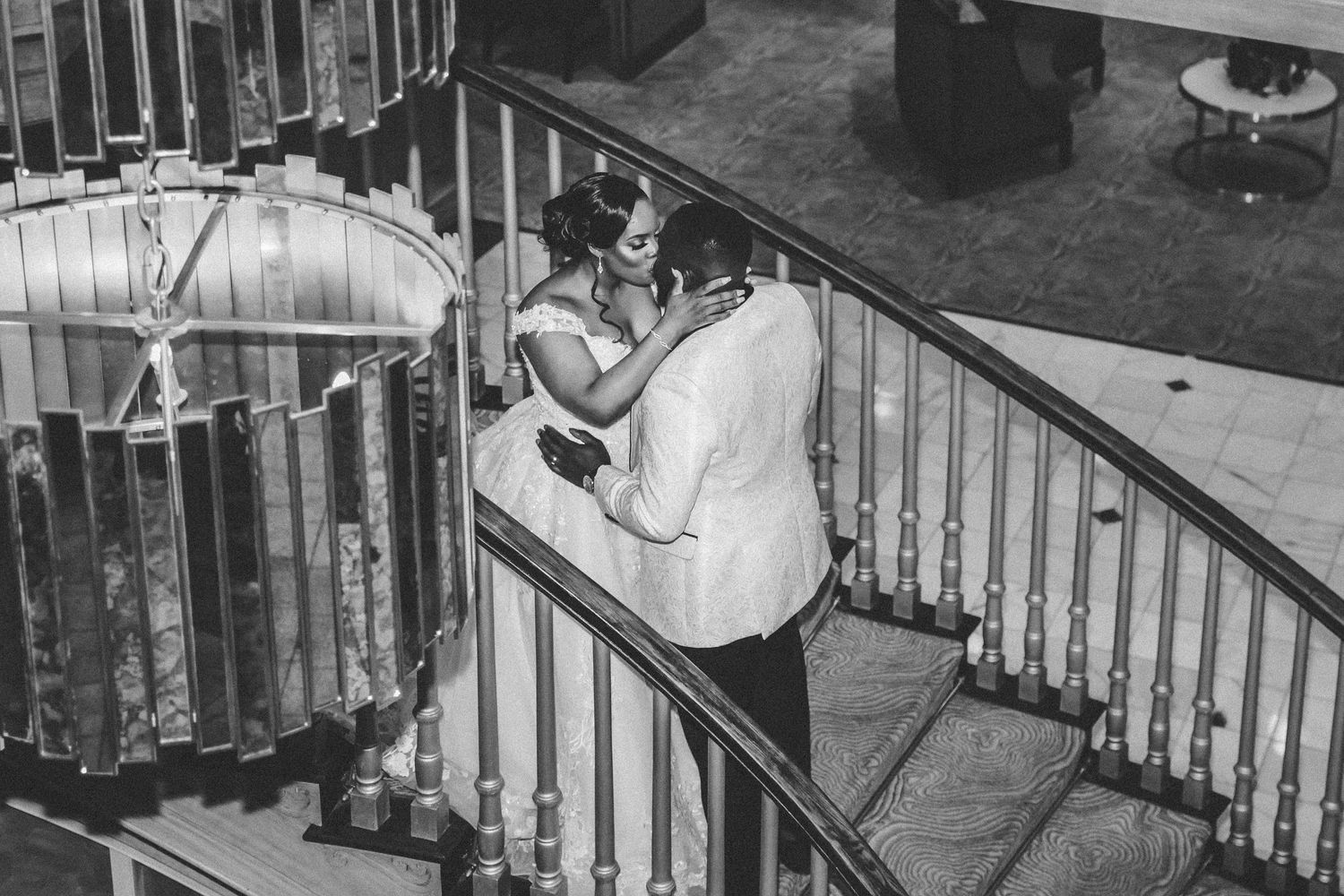 Black and white photo of bride and groom sharing a tender embrace on a grand staircase at wedding venue.