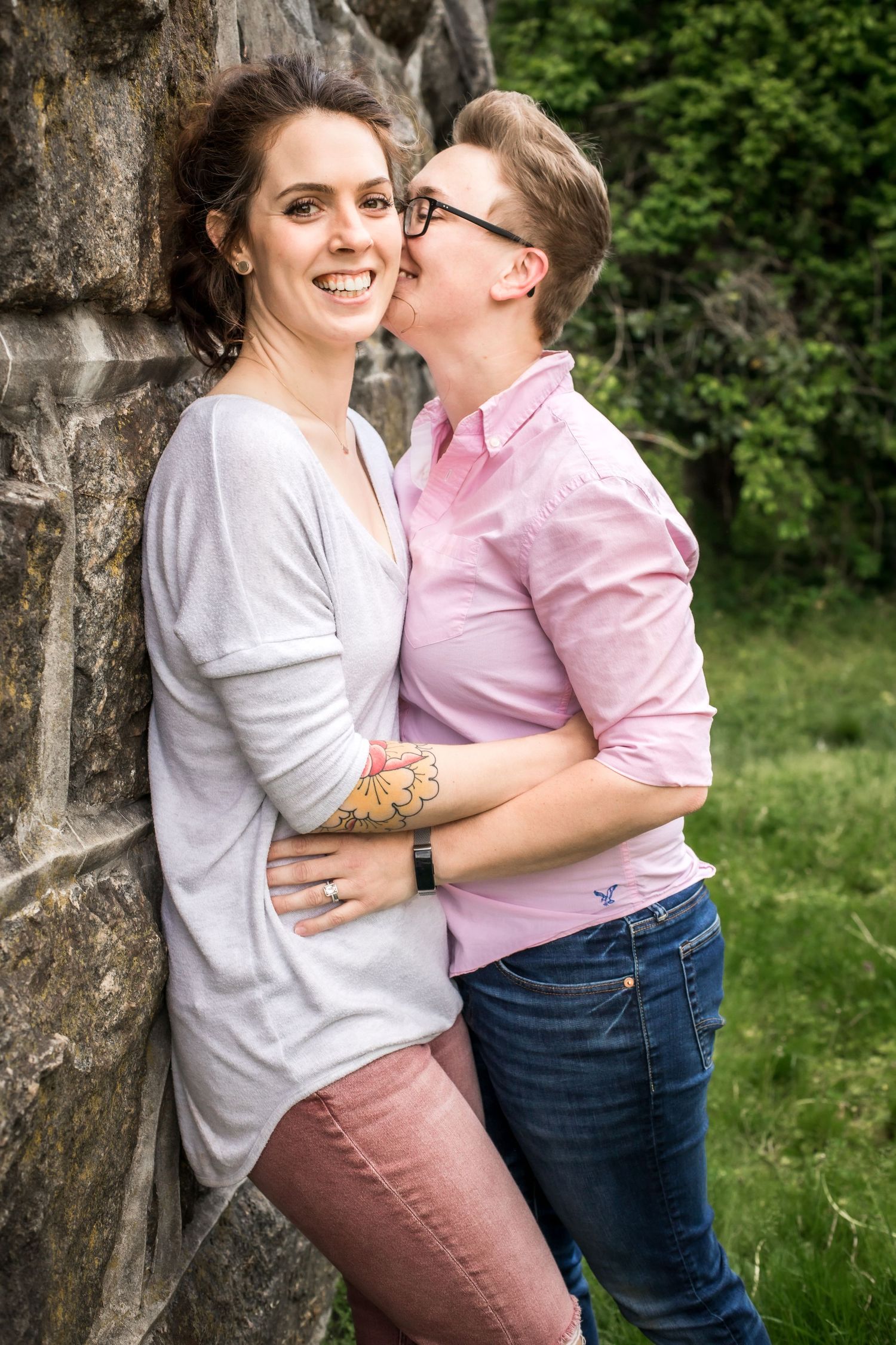 Couple sharing intimate moment against stone wall in casual spring outfits.