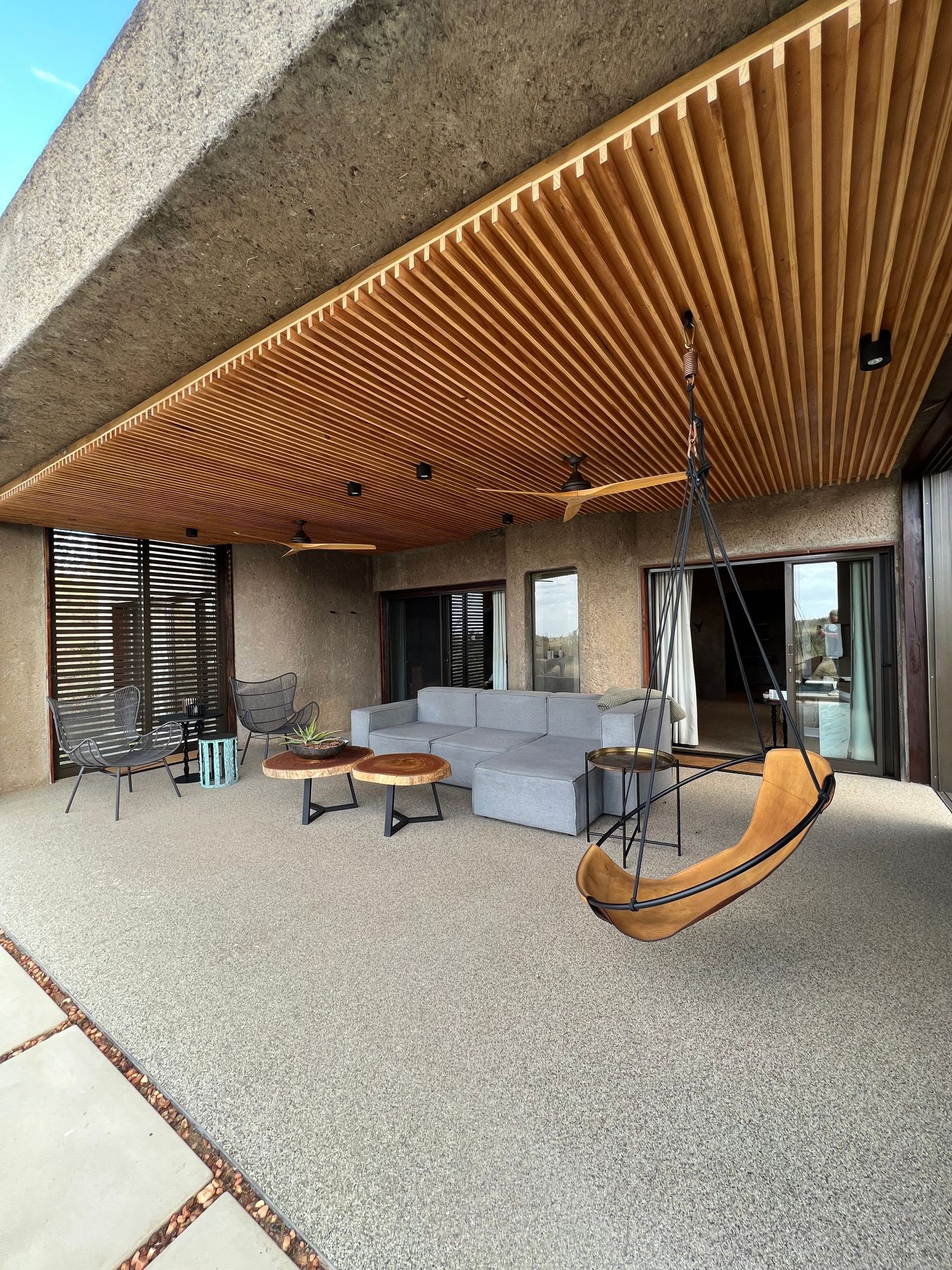 Contemporary covered patio with wooden slatted ceiling and modern outdoor furniture including a hanging chair.