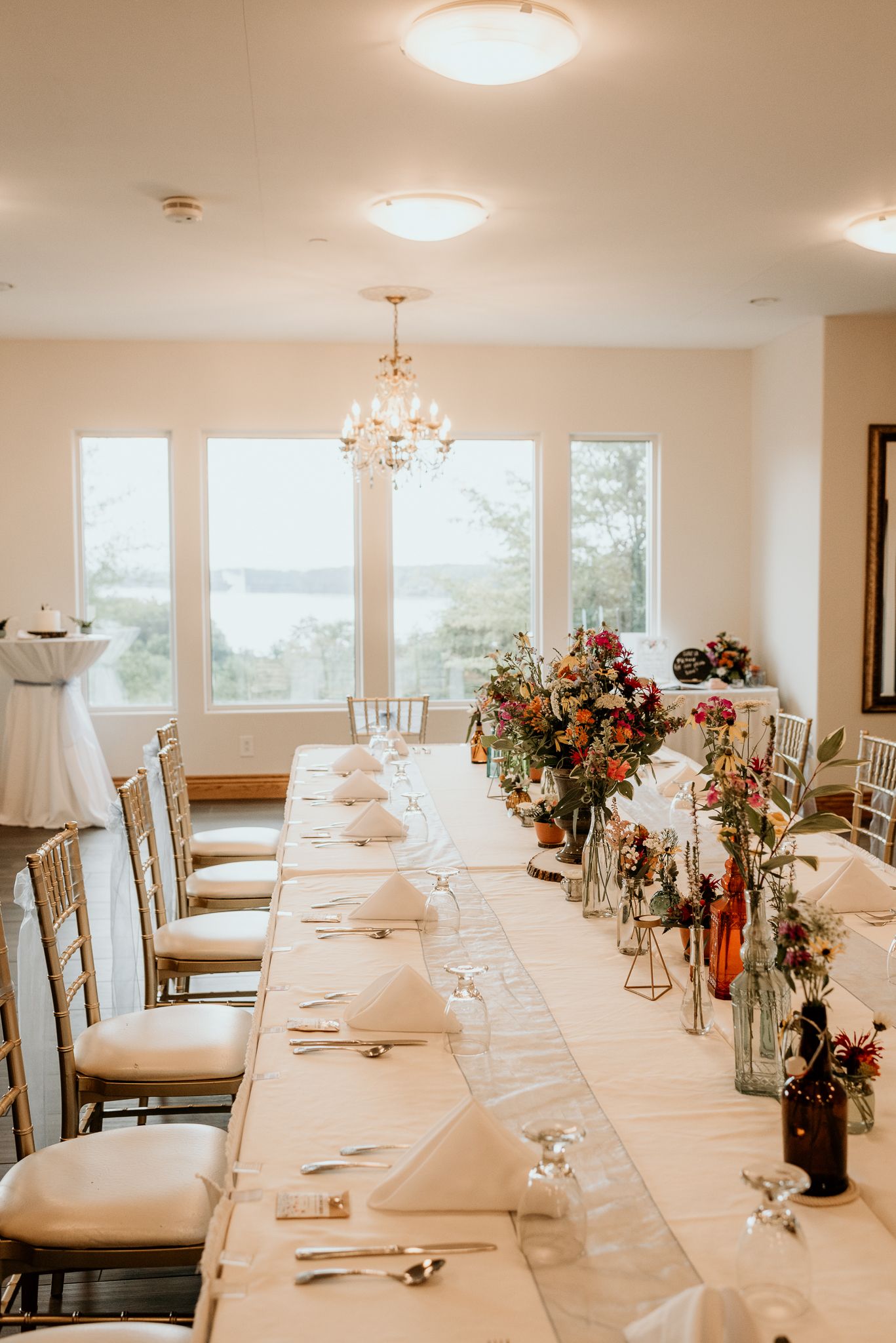 Long white dining table set for a formal wedding reception with elegant centerpiece decorations.