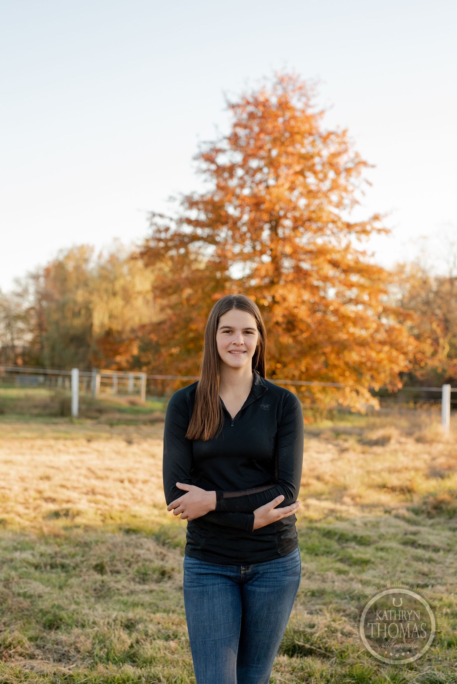 Portrait against vibrant orange fall foliage with rustic fence in background.
