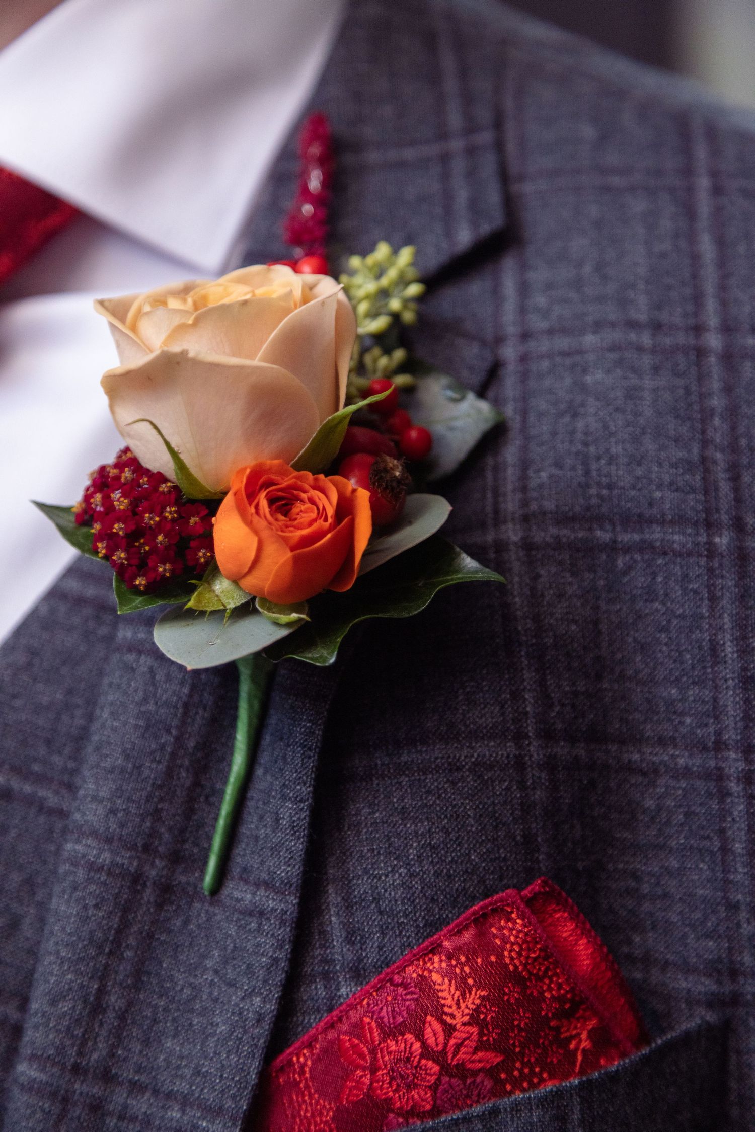 A boutonniere with peach and orange roses against a gray checkered suit jacket.