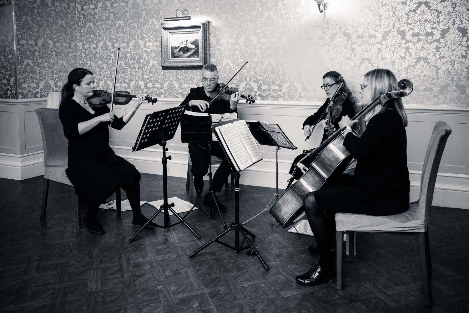 String quartet performs music in an elegant room with floral wallpaper and hardwood floors.