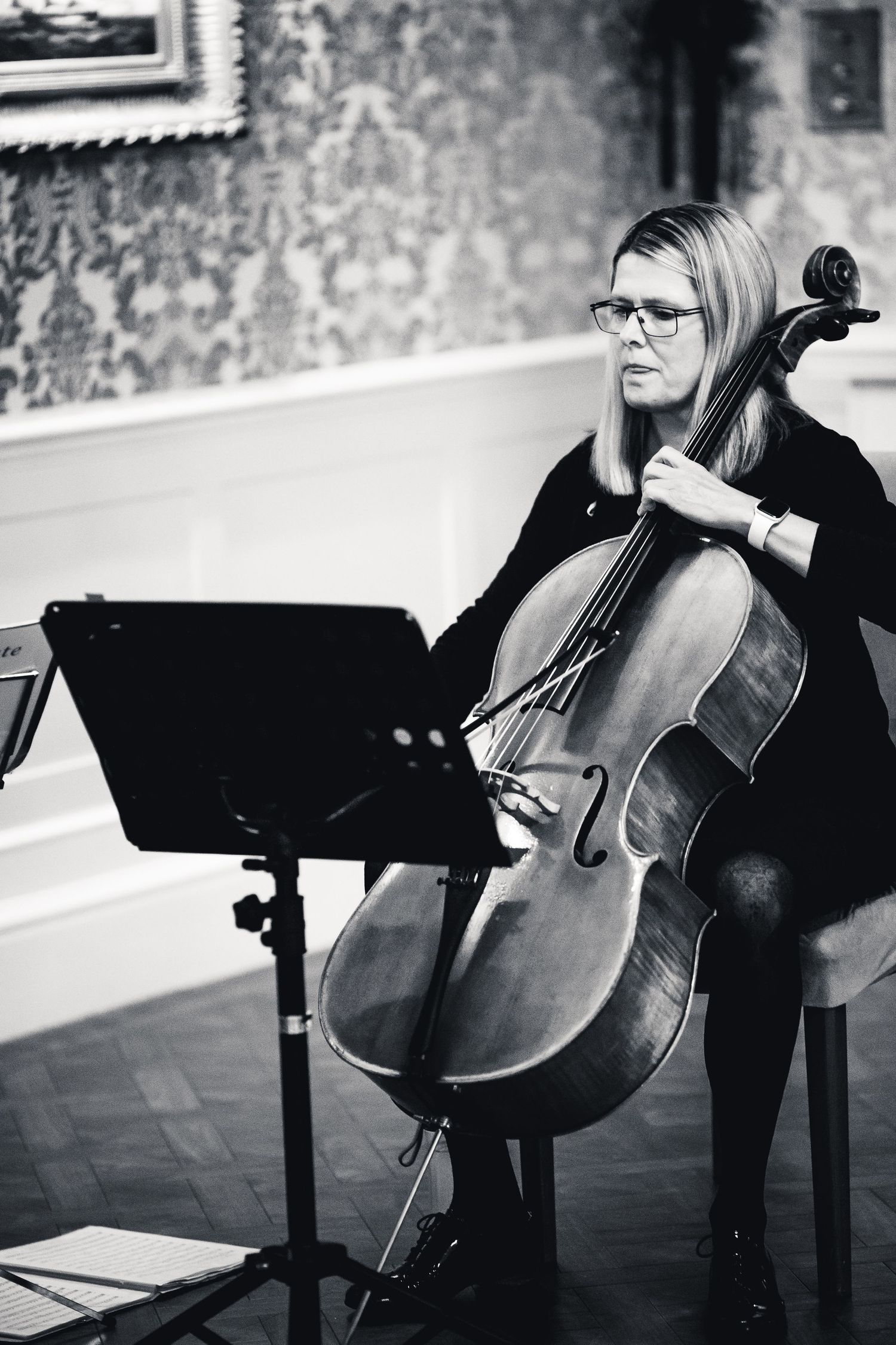 Professional cellist performs with sheet music during a classical music recital in an elegant venue.