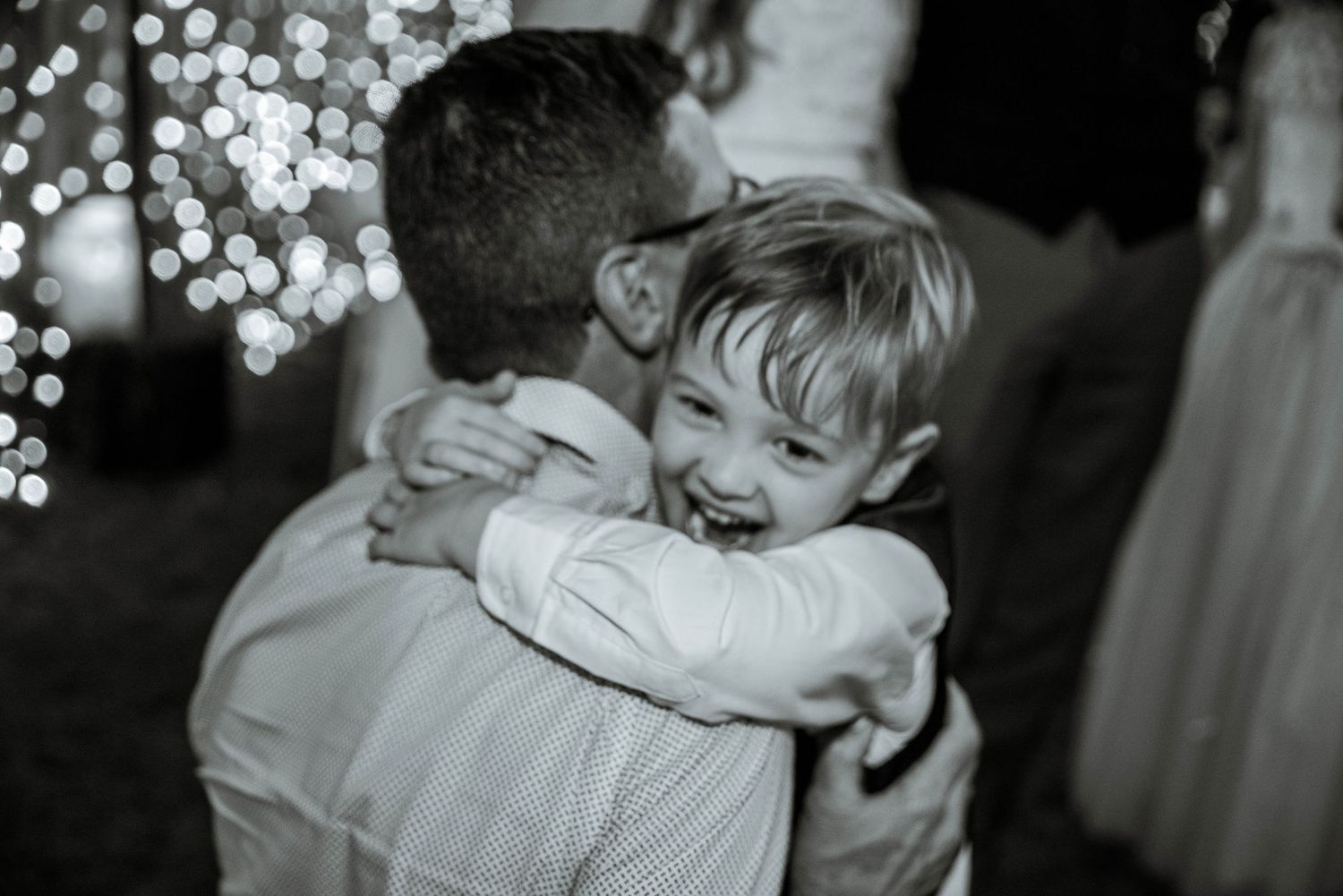 Black and white emotional moment captured with twinkling lights in background.