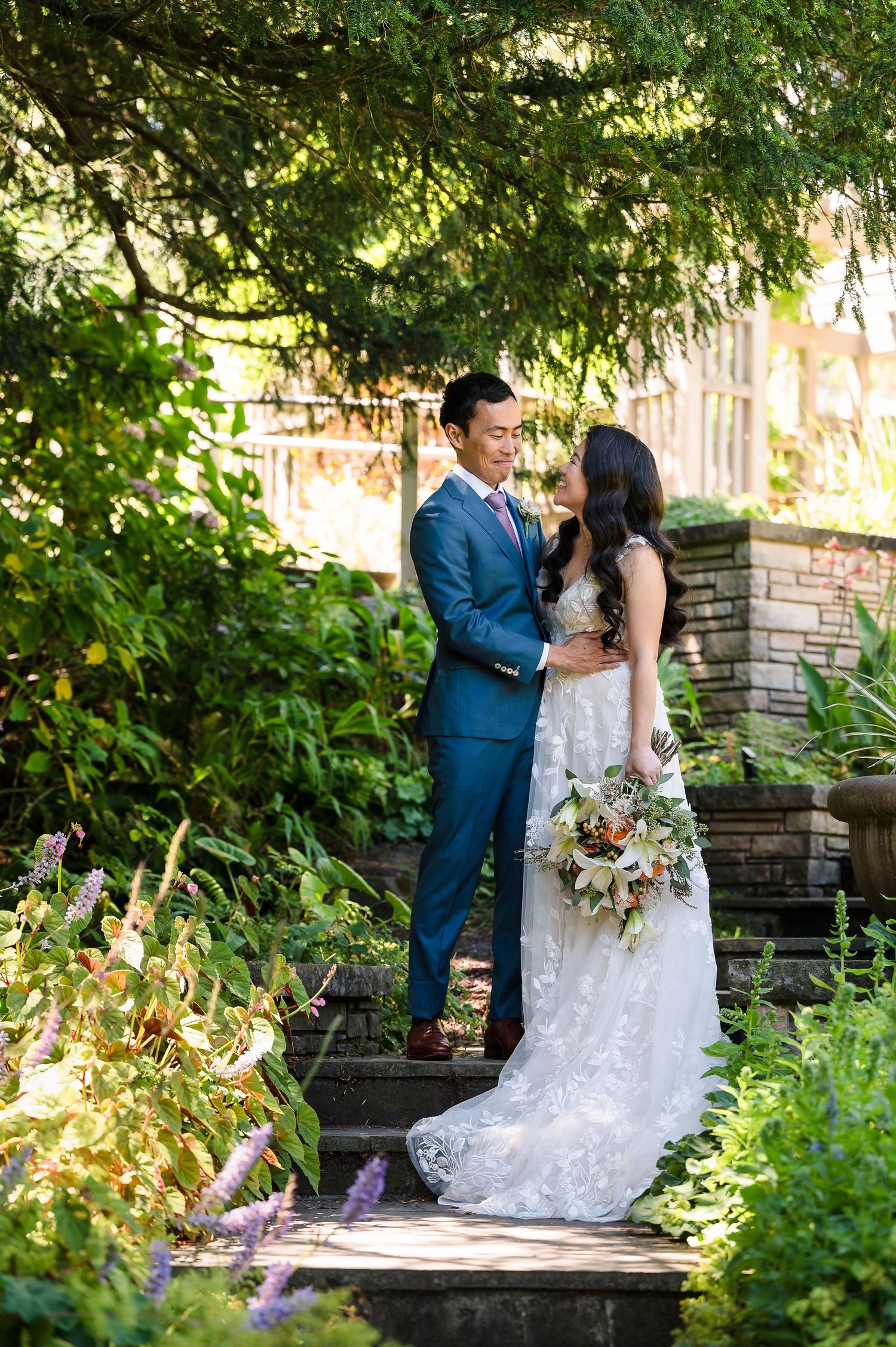 A couple shares an intimate moment on garden steps surrounded by lush greenery.