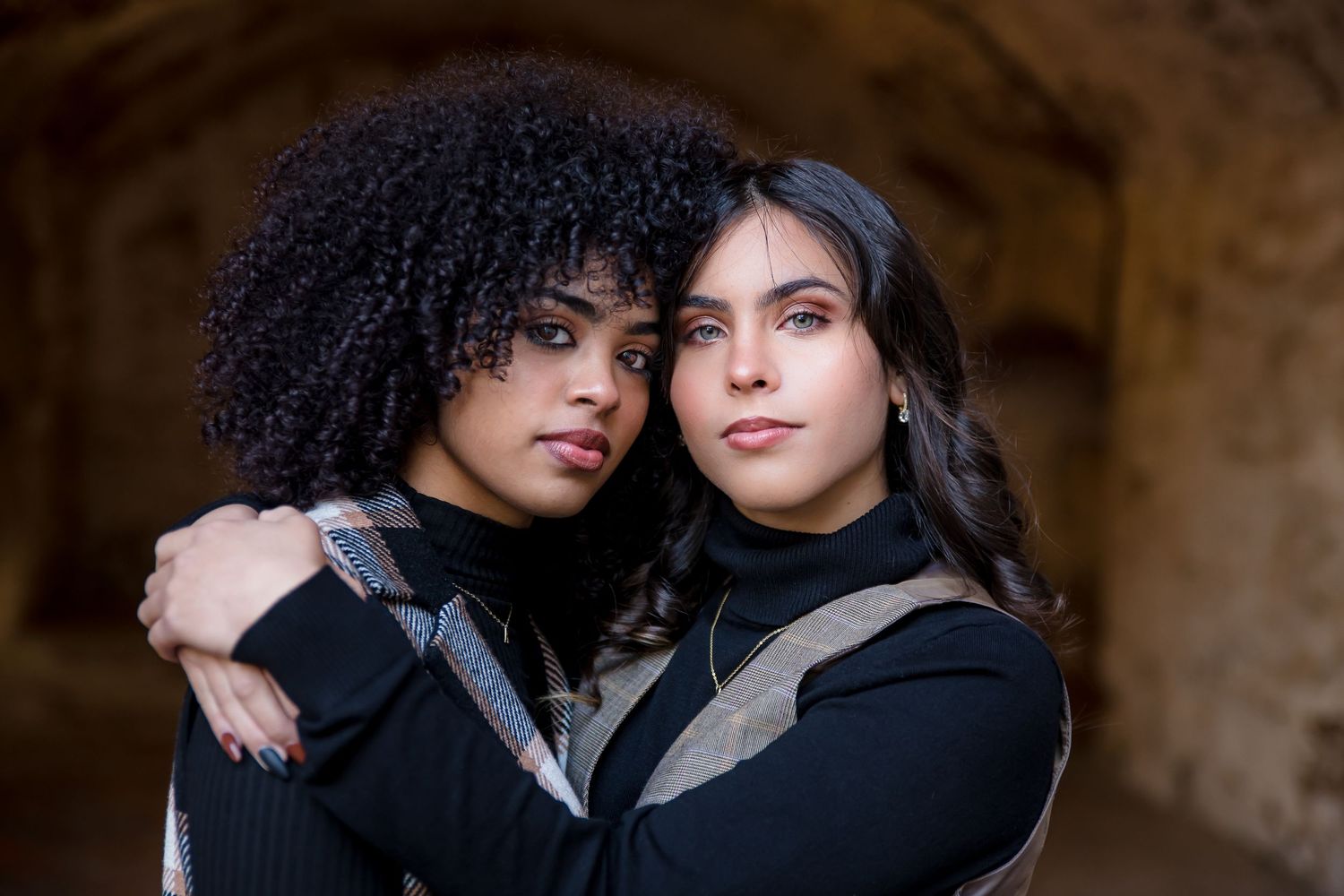 Two people in dark outfits sharing an intimate moment against a stone wall background.