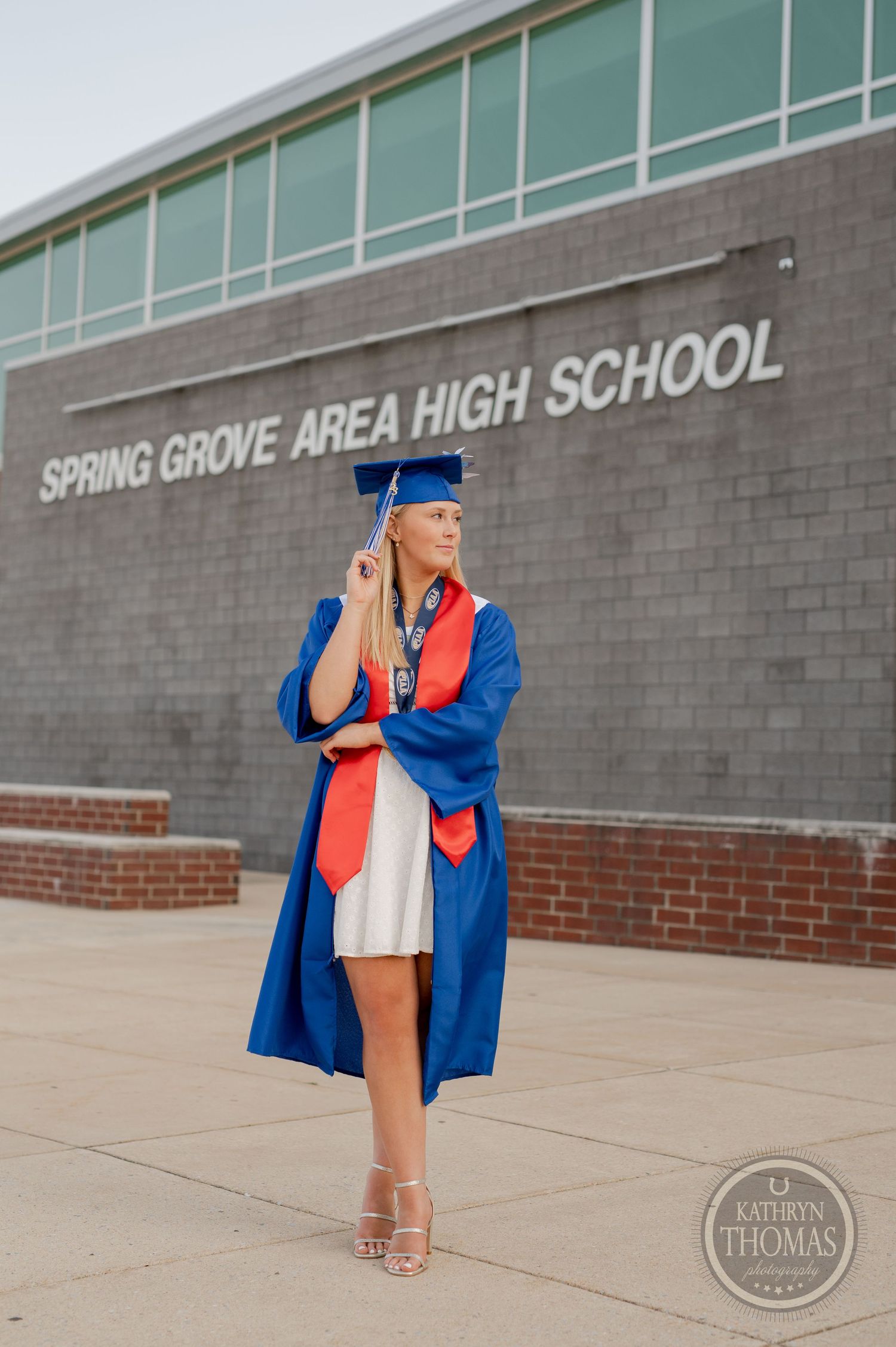 Graduate poses in blue cap and gown outside Spring Grove Area High School entrance.