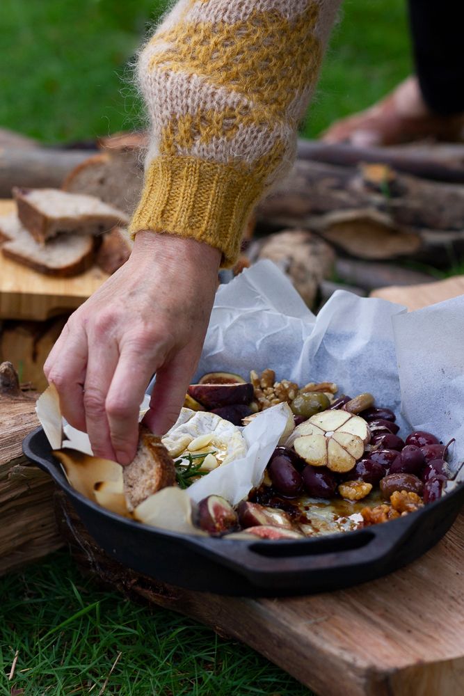 Event photo of hand reaching for gourmet cheese platter with grapes, nuts, crackers, outdoor picnic charcuterie board on wooden serving tray