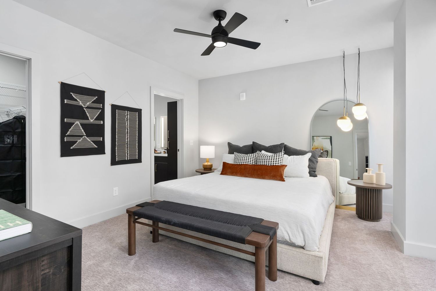 Downtown Columbus Ohio apartment bedroom interior with white walls, geometric wall art, ceiling fan, and plush bedding in neutral tones.