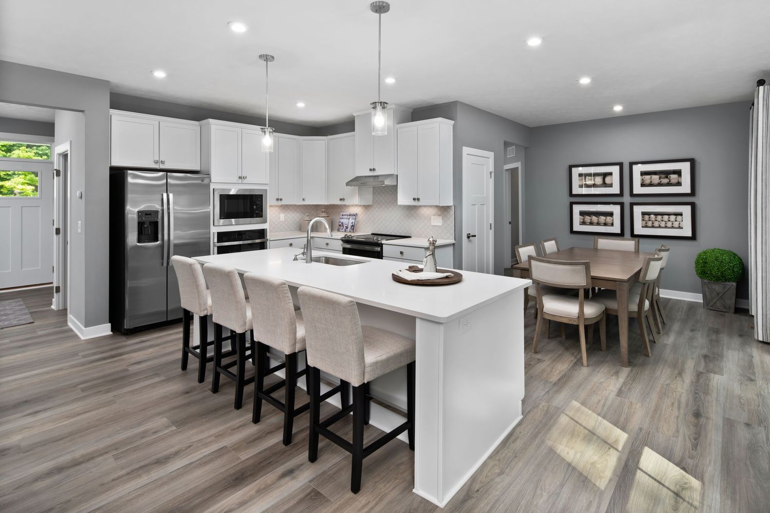 Model home open-concept kitchen with white cabinets, gray walls, quartz island, and hardwood floors features bar seating and a dining area.