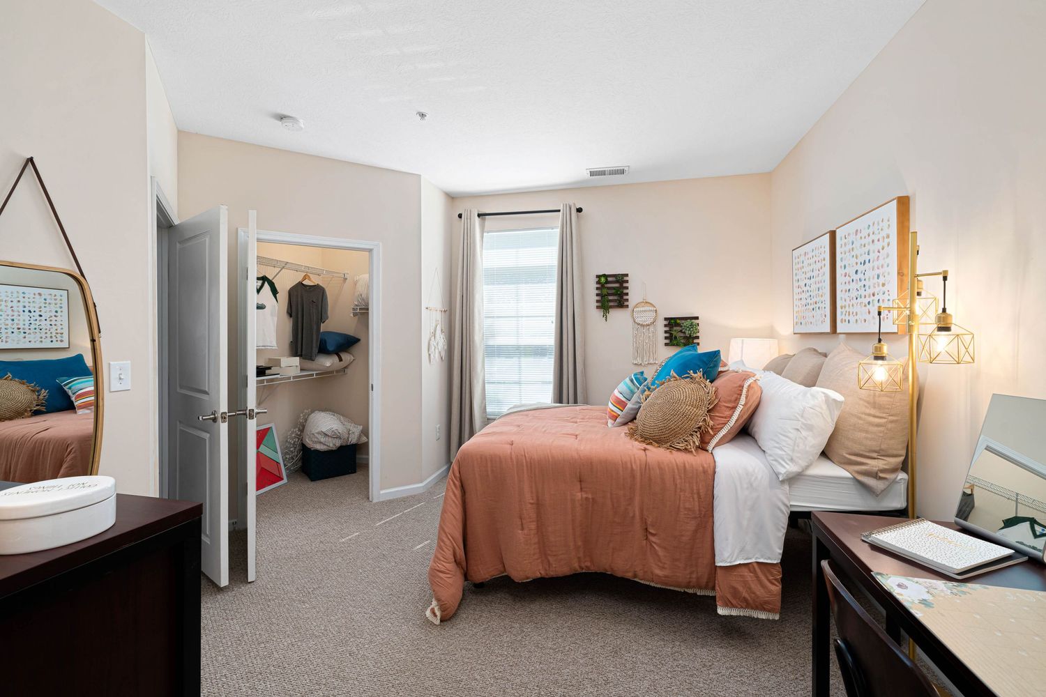 Modern student apartment bedroom with coral bedspread, white walls, and gray carpet showcases compact living space.