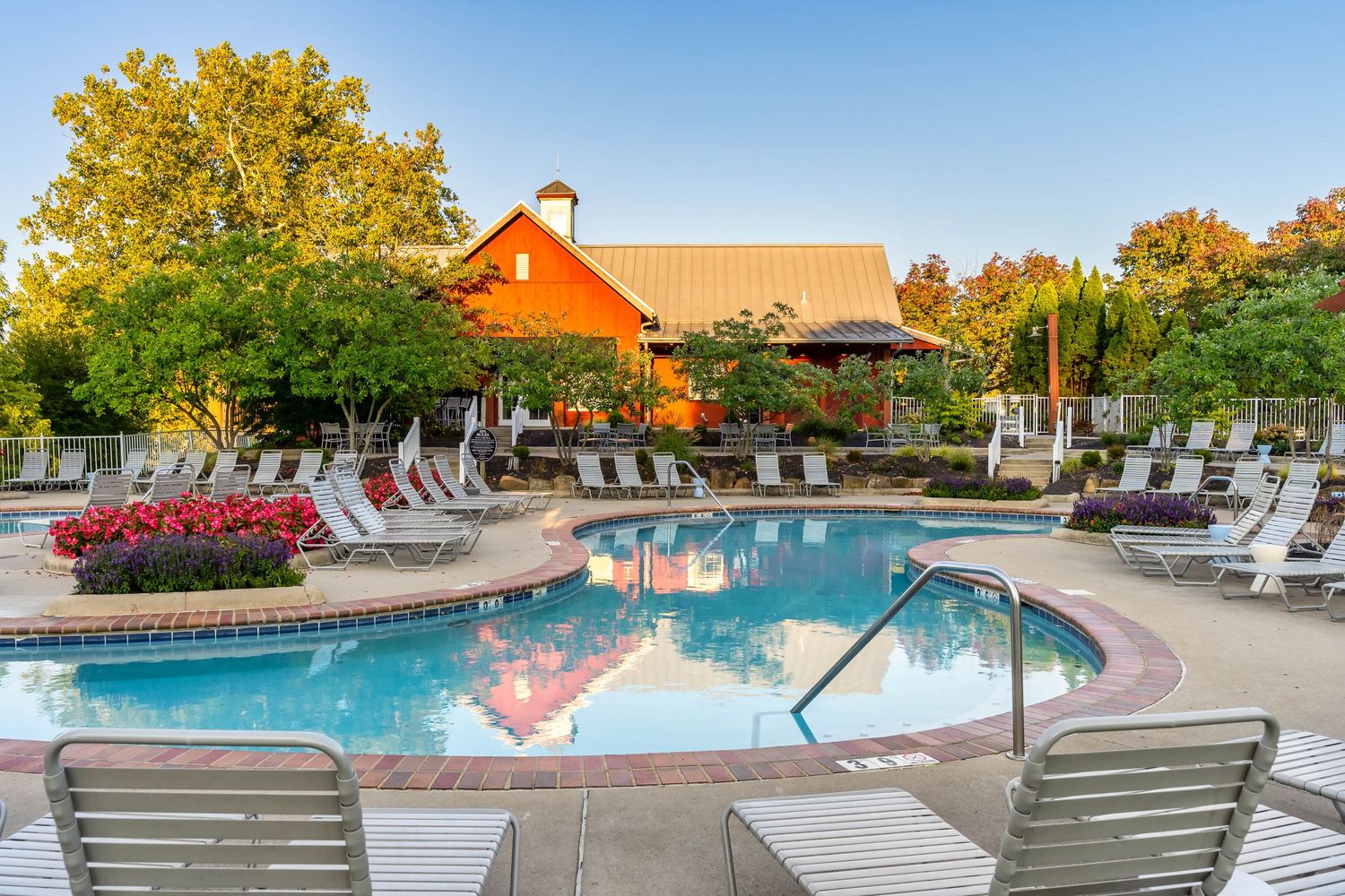 A resort multi-family apartment pool area with lounge chairs surrounded by colorful fall foliage and a red barn clubhouse in the background.