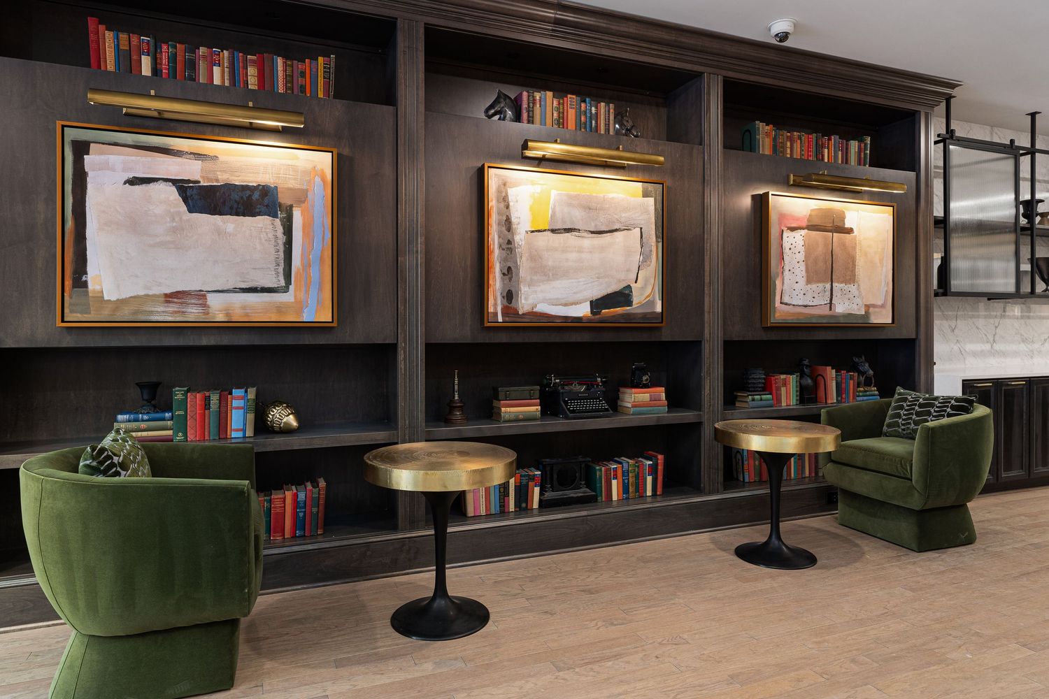 Columbus apartmet lounge area with dark built-in shelving, illuminated artwork displays, green velvet chairs and round bistro tables.
