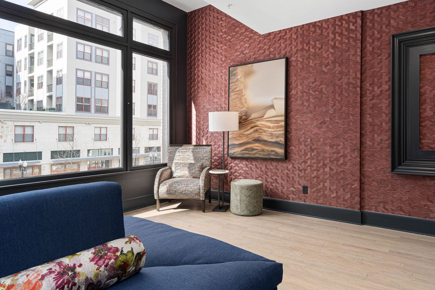 Downtown Columbus Ohio apartment clubroom with red brick wallpaper, navy sofa, accent chair, and large window overlooking urban buildings.