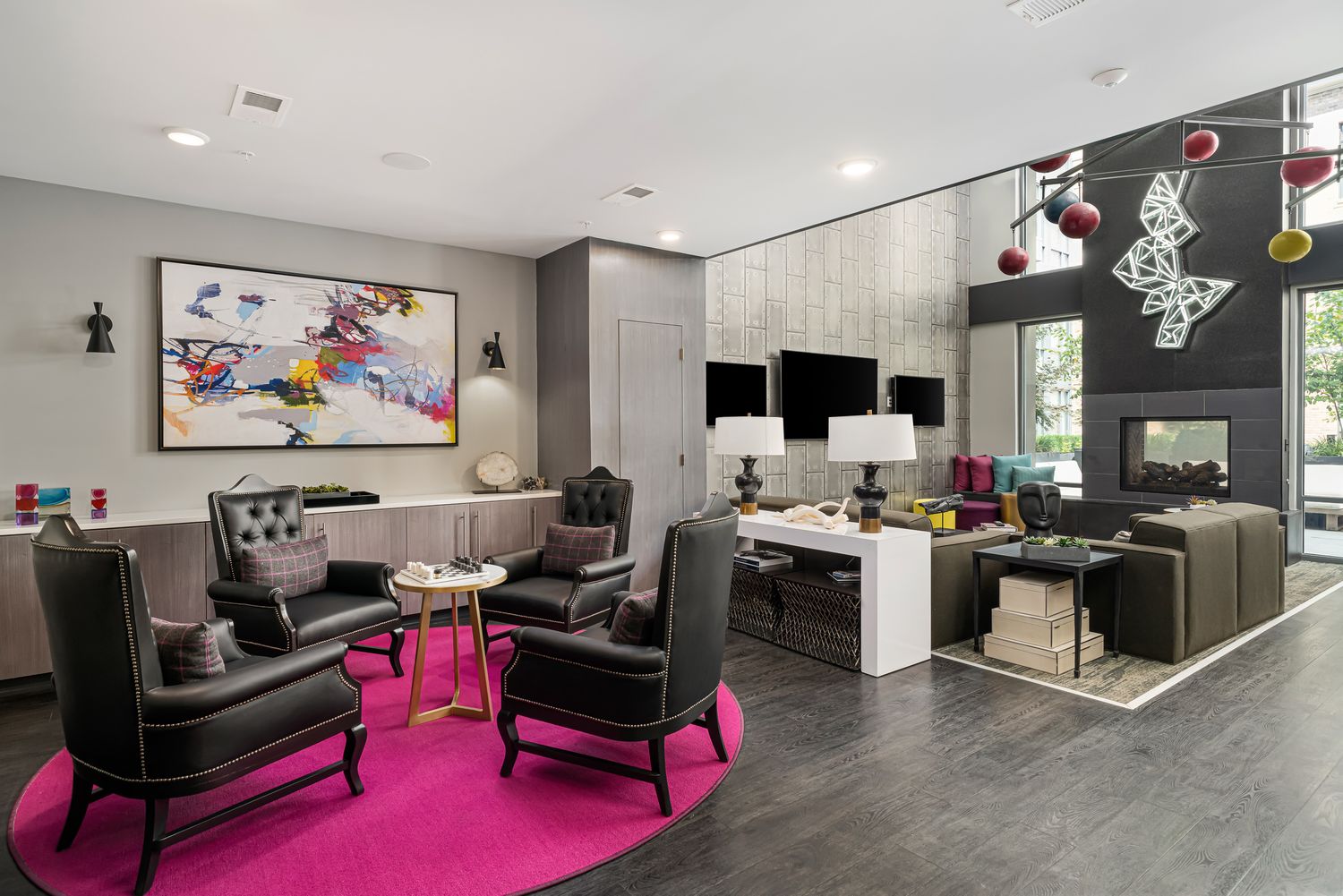 Modern apartment clubroom lounge area with pink carpet, black chairs, white workstations and colorful wall art in contemporary setting.