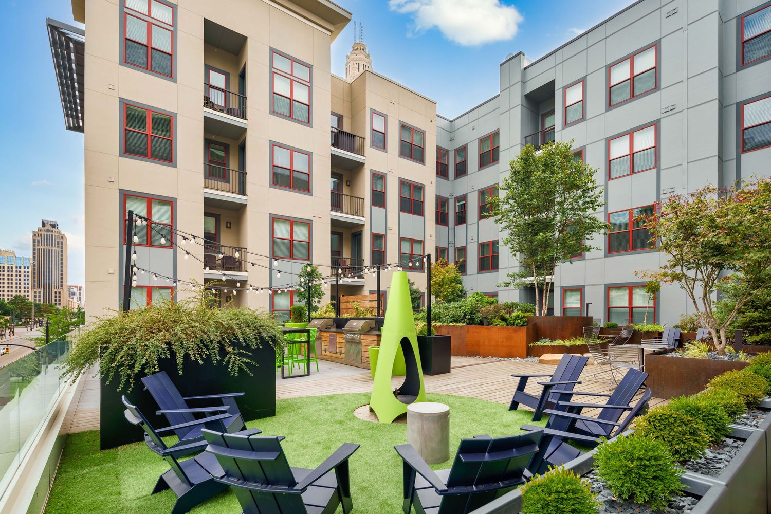 Downtown apartment building courtyard featuring blue Adirondack chairs and artificial turf with urban architecture backdrop.